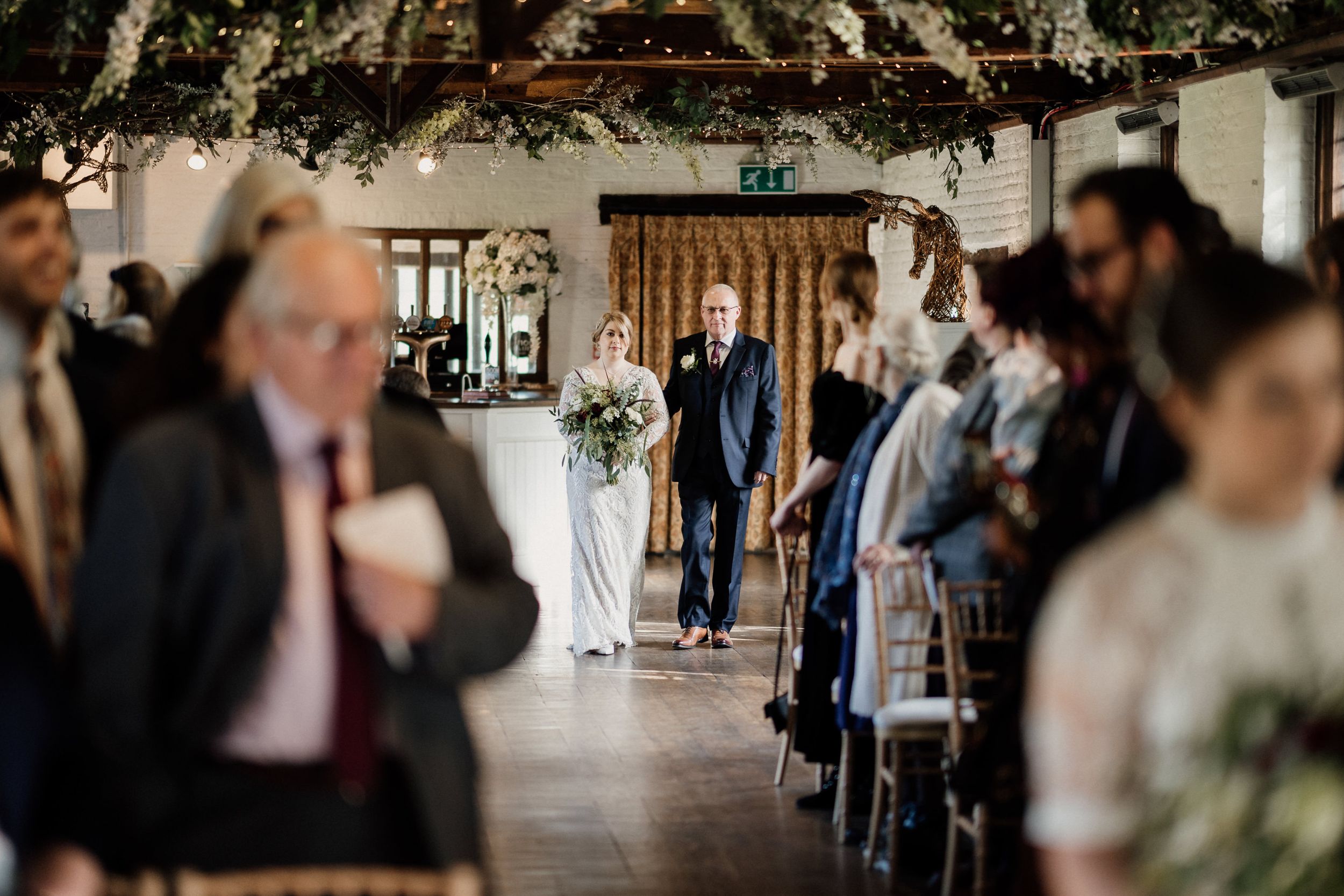 Wedding ceremony processional in rustic venue with gathered guests.