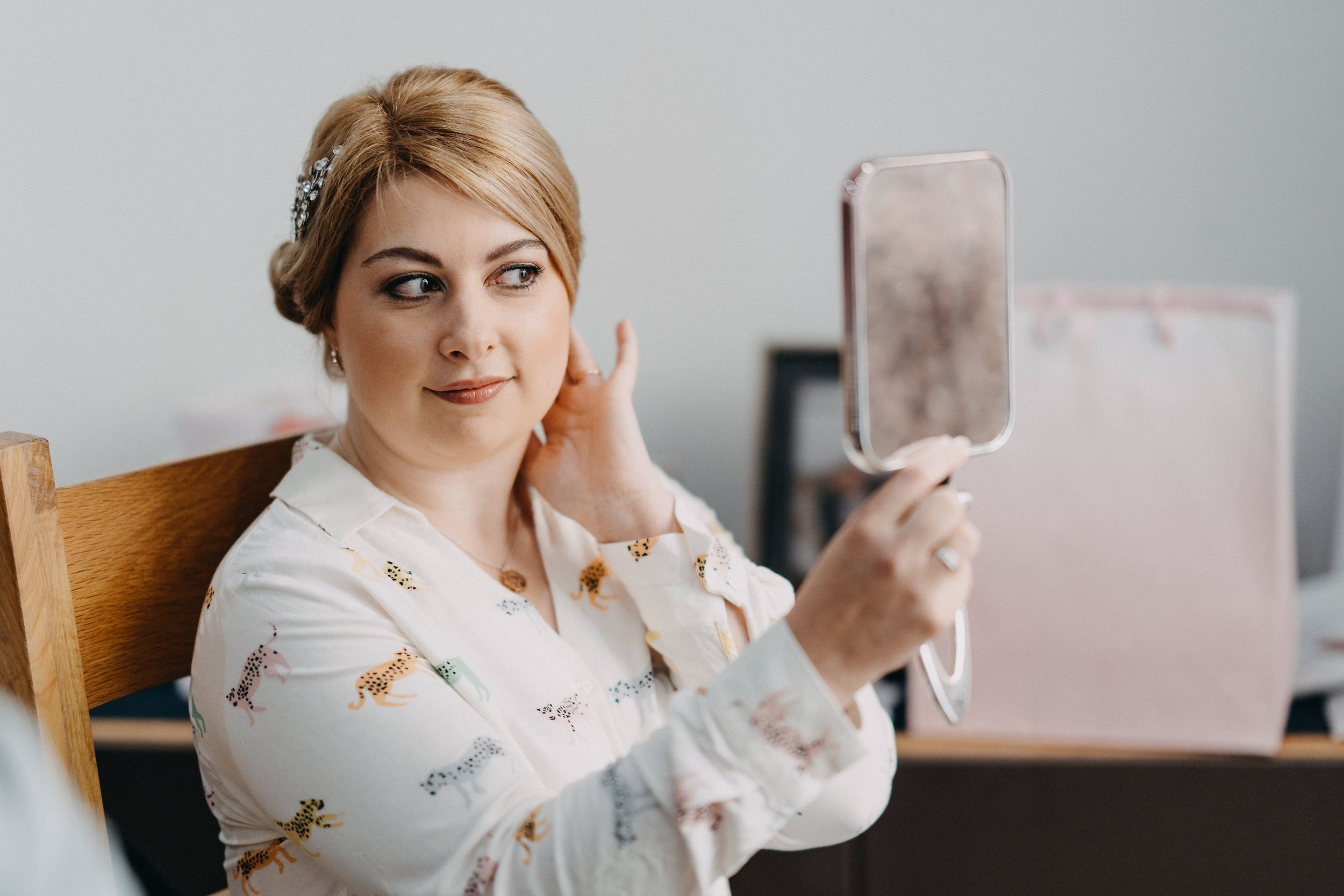 A person in a floral robe looking at their reflection in a handheld mirror.