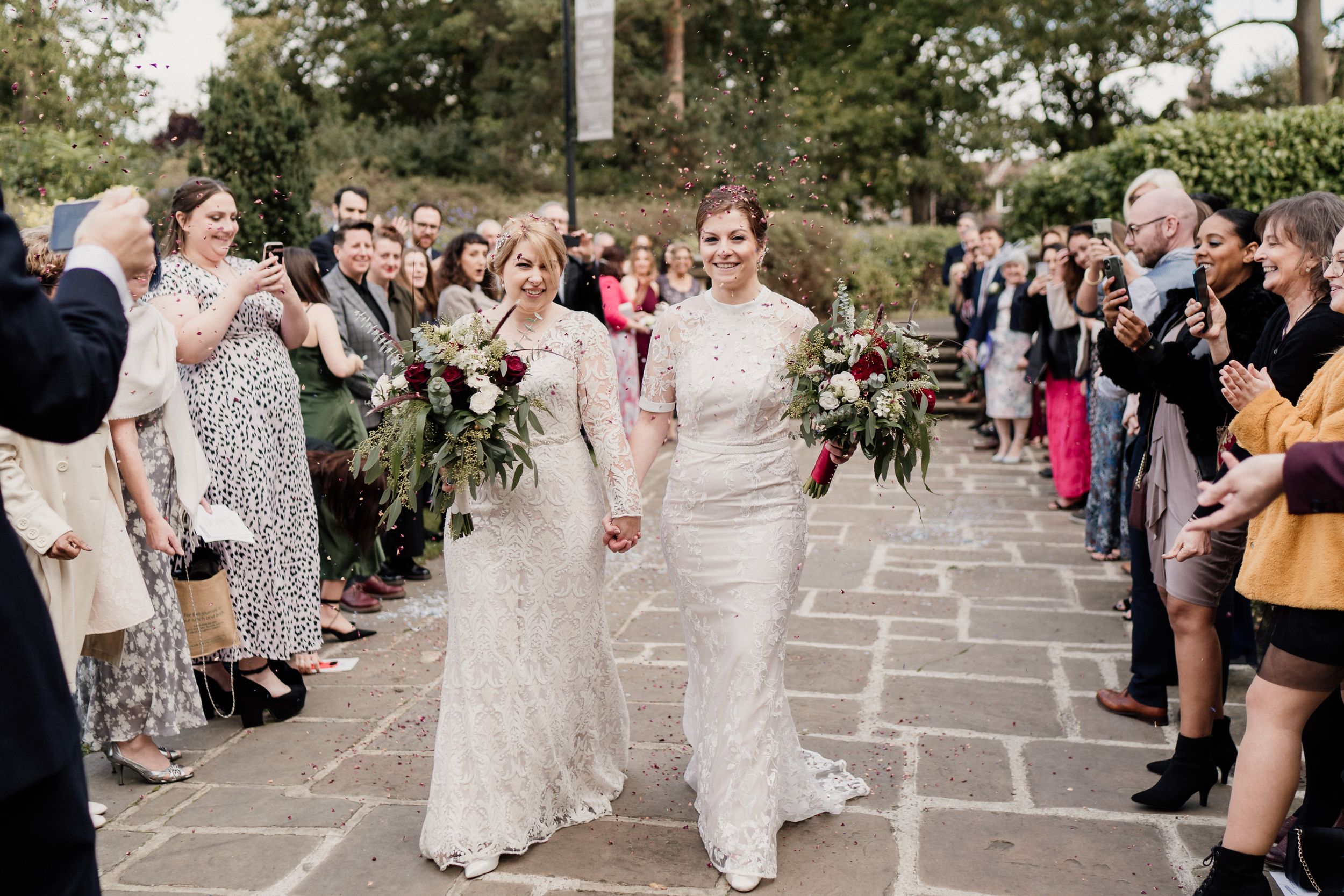 Wedding couple walks down stone pathway as guests line both sides in celebration.