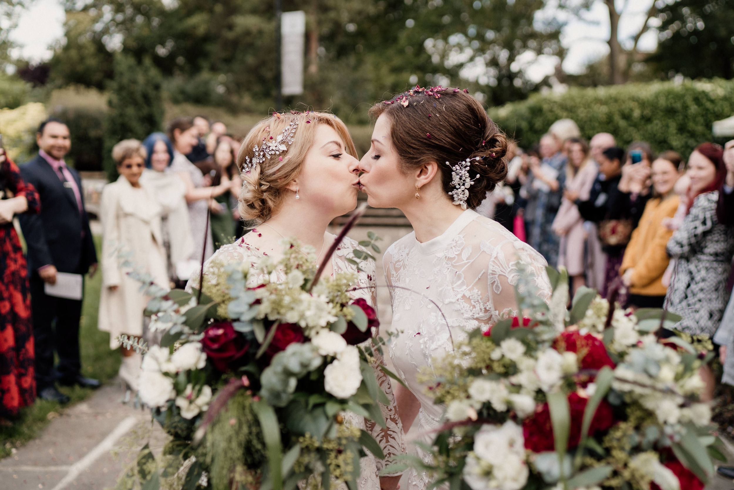 Newlyweds share romantic kiss while holding elegant bouquets of roses and greenery of Tudor Barn Eltham.