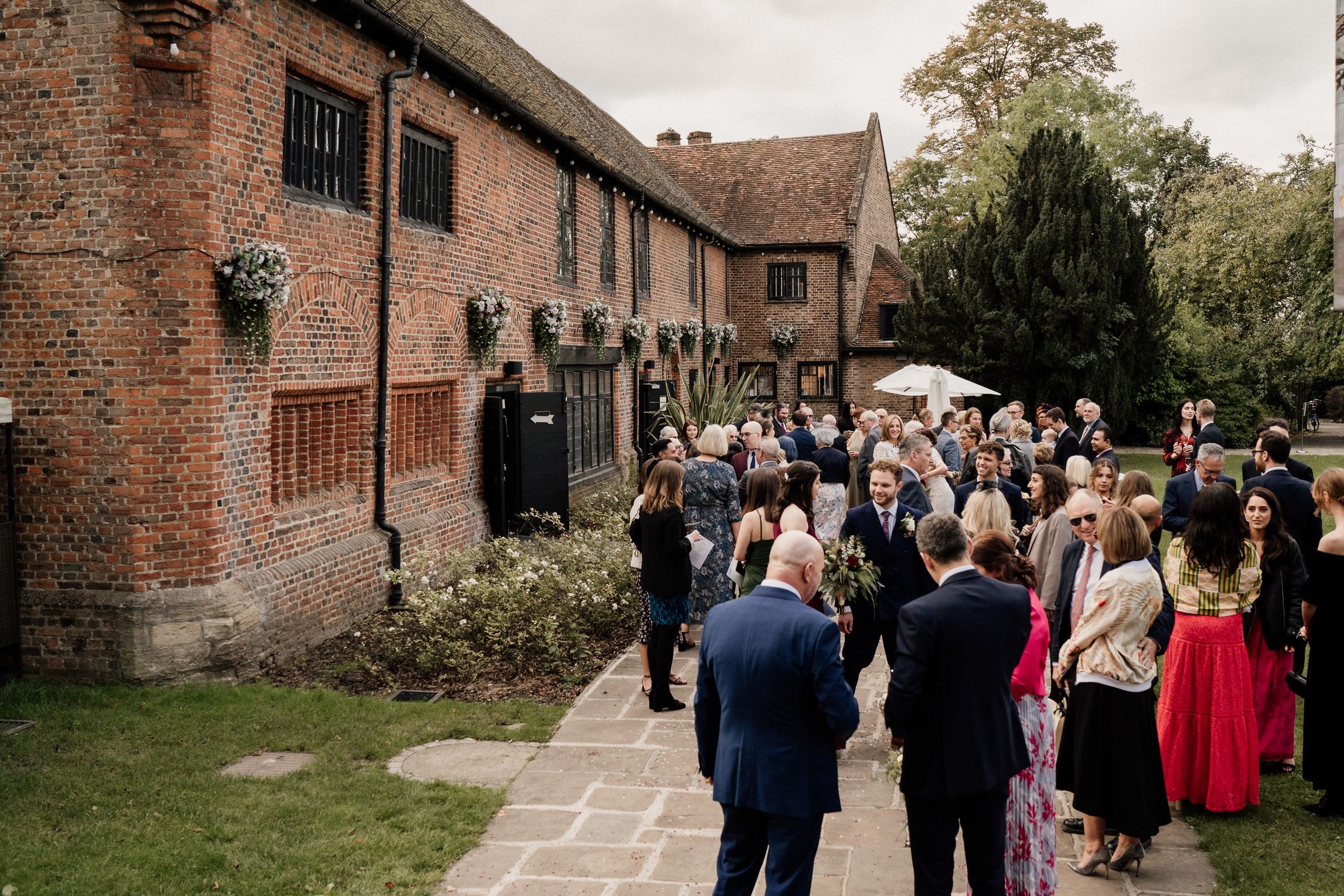 Wedding guests gather outside historic brick building during reception at Tudor Barn London.