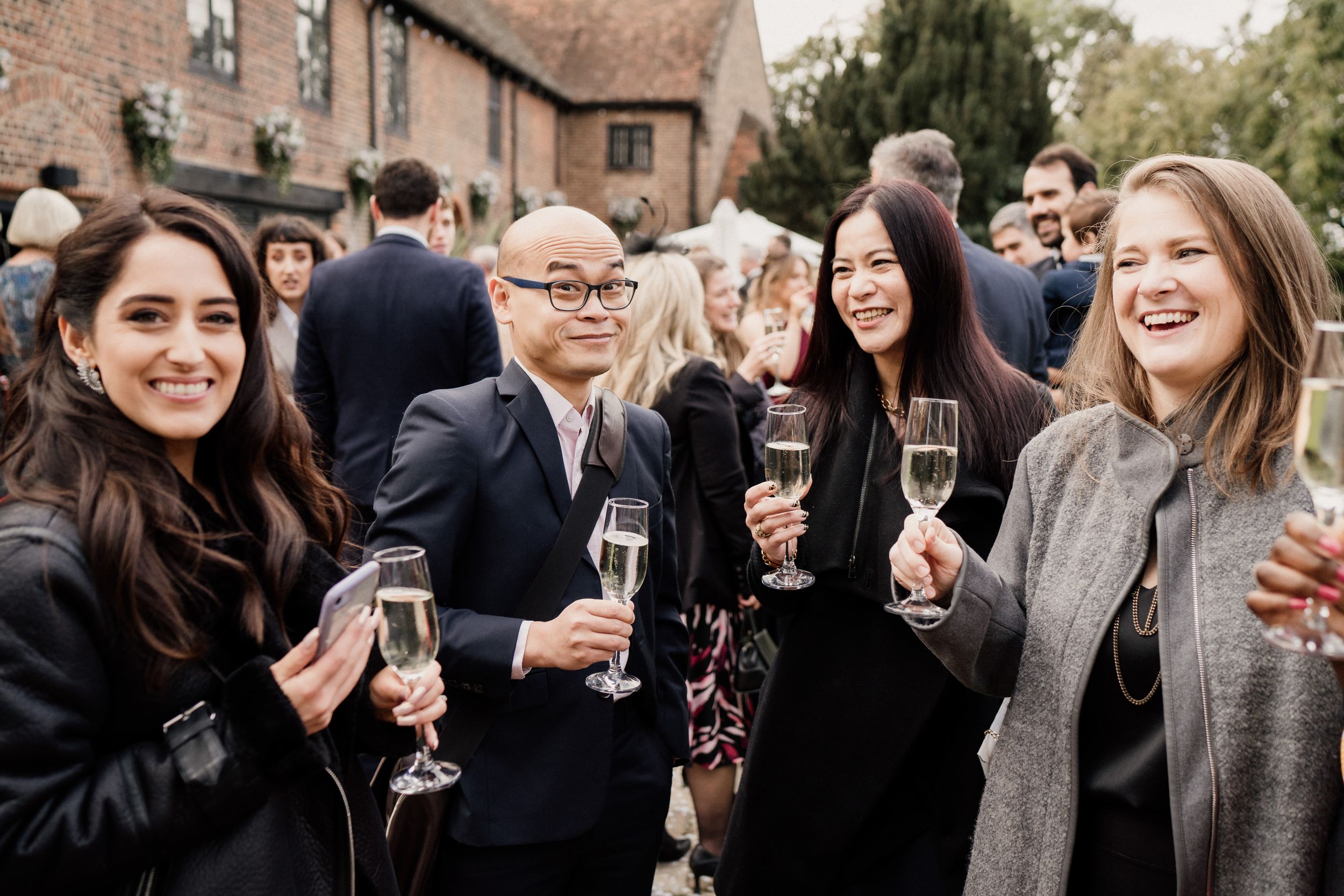 Group of wedding guests smile while holding champagne glasses at outdoor celebration.
