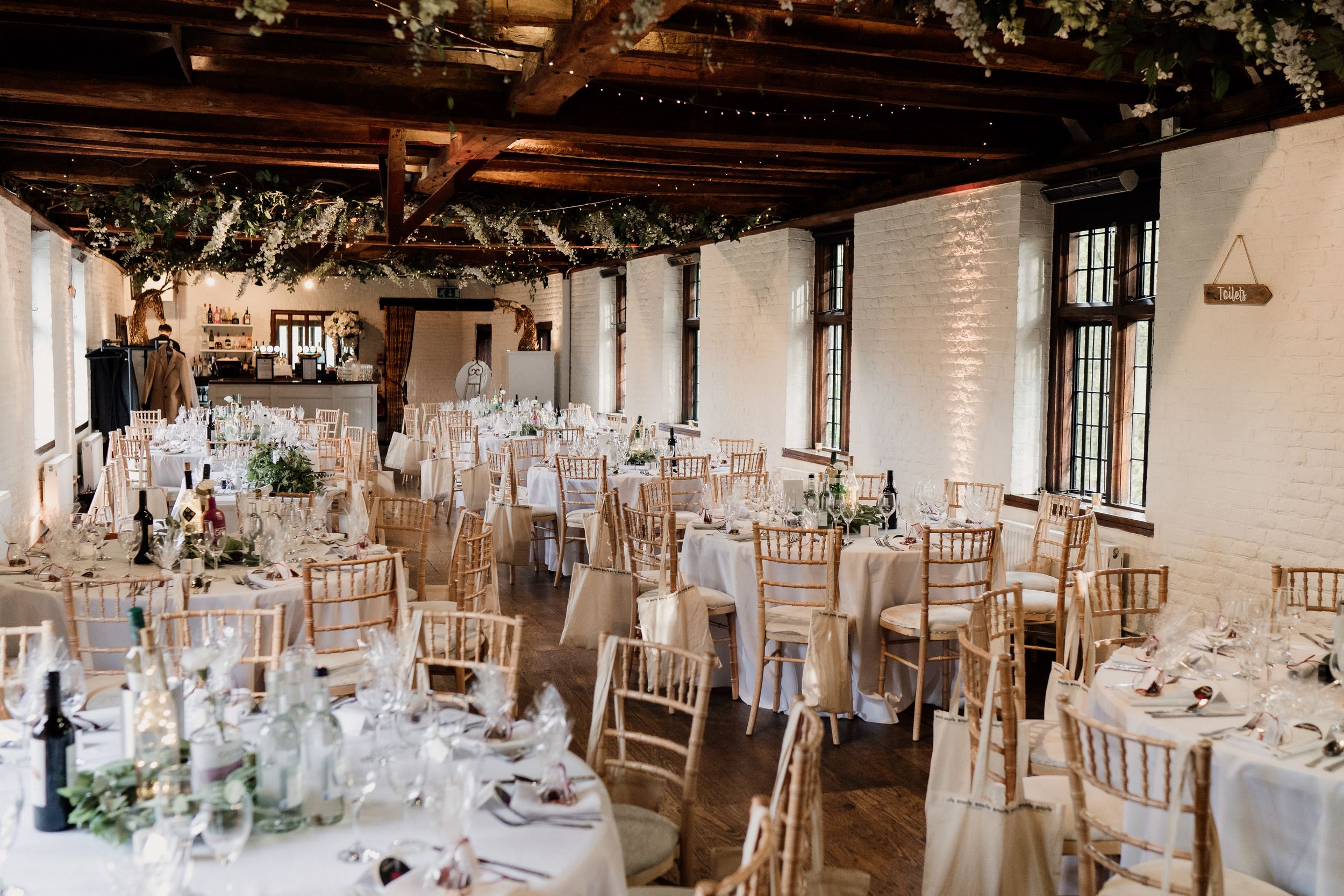 An elegant wedding reception at Tudor Barn setup with white decor and floral arrangements in a rustic indoor venue.