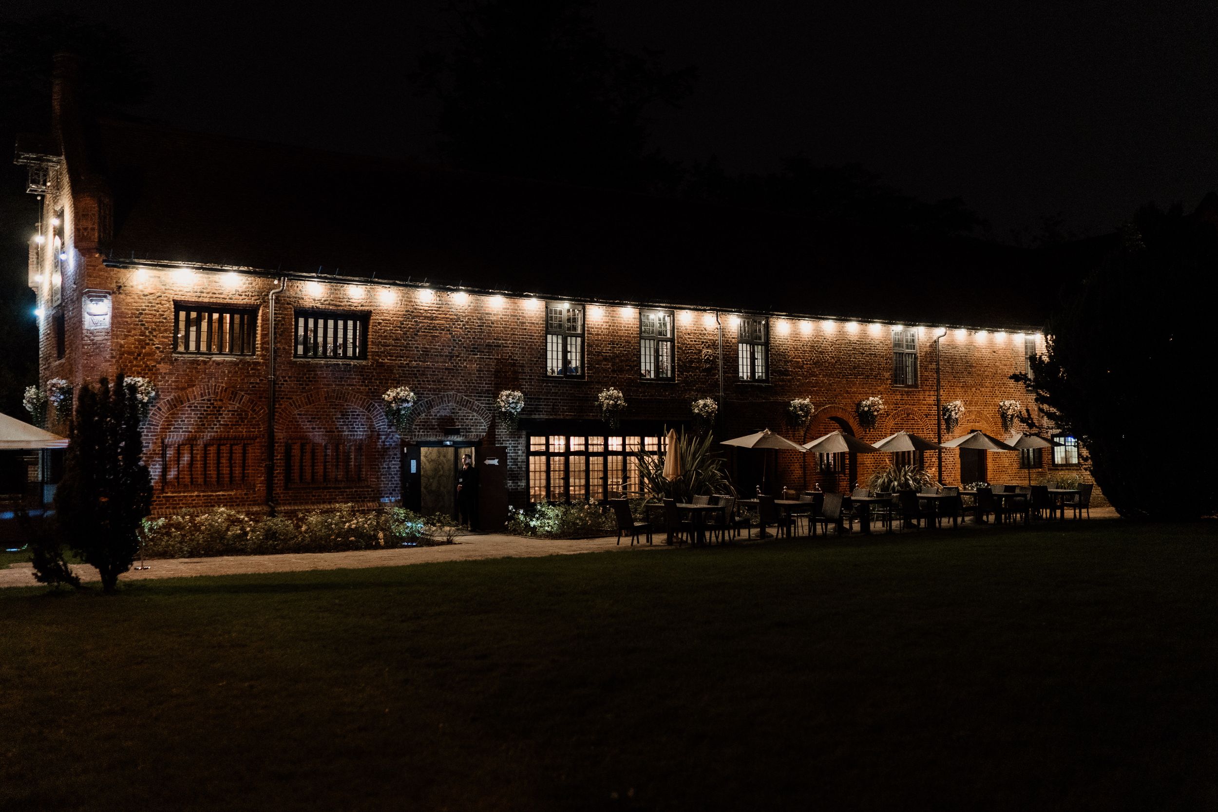 A historic brick building of Tudor Barn Eltham illuminated at night with string lights creating a warm ambiance.