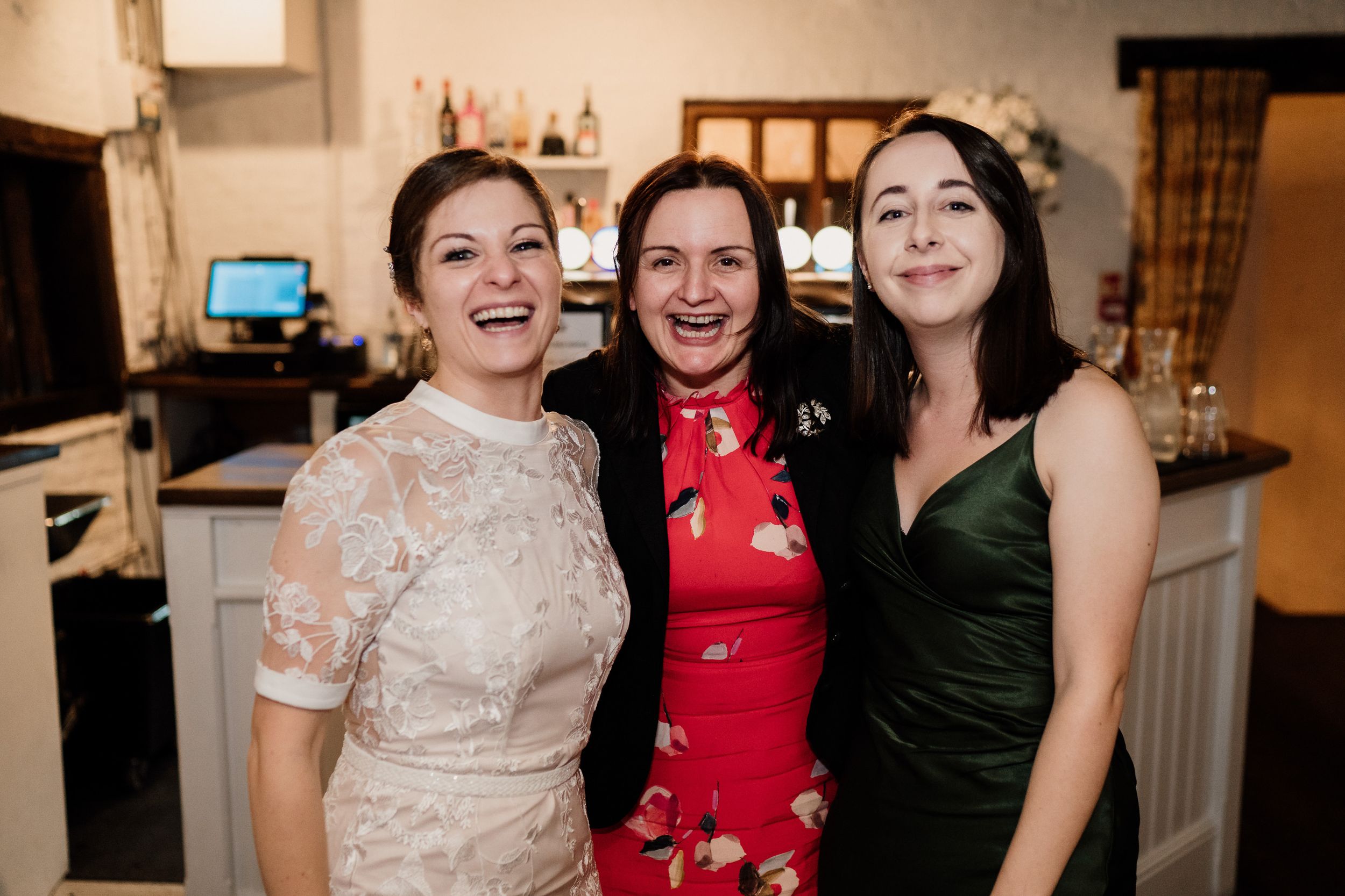 Three people pose together at a celebration, wearing formal attire in lace, red, and emerald green.