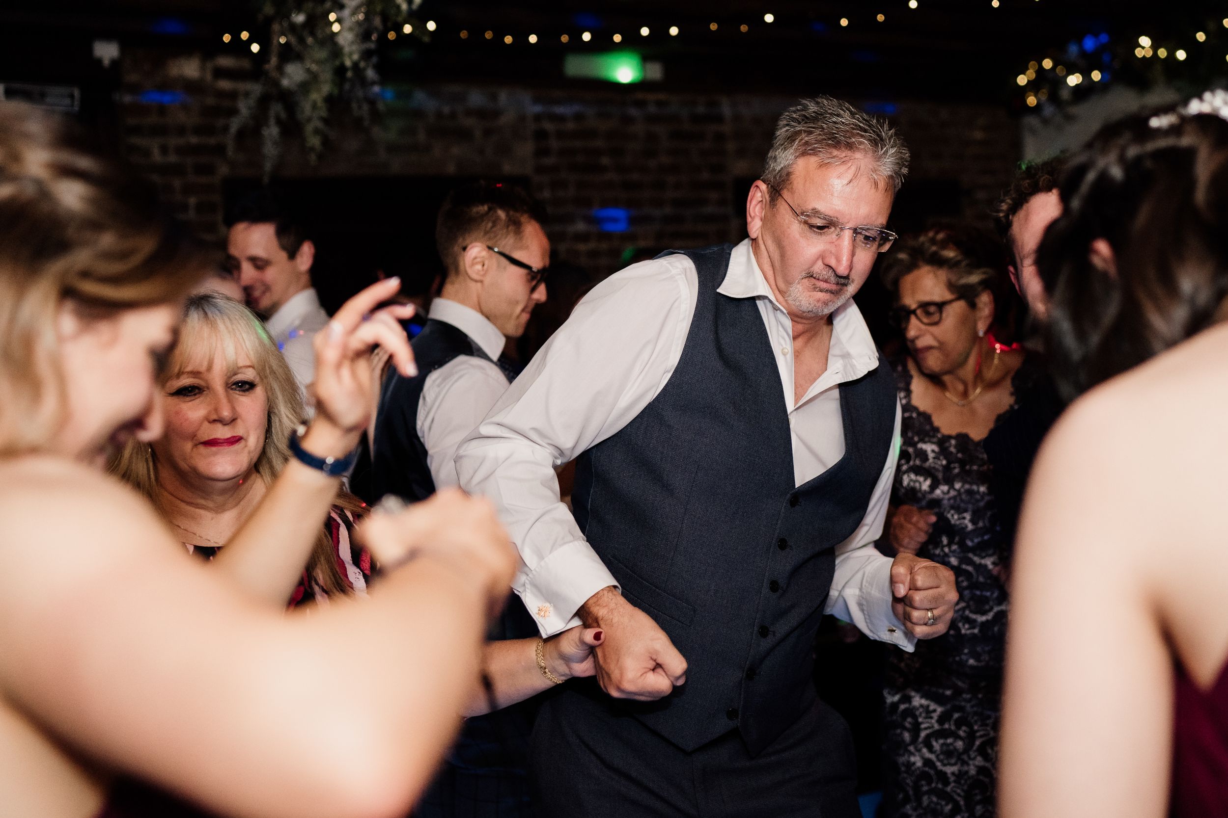 Wedding guests dancing and celebrating on a dimly lit dance floor.