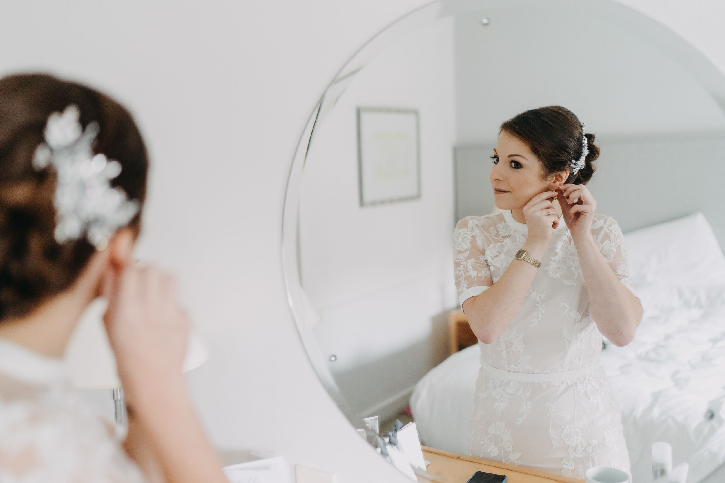A reflection in a mirror shows someone adjusting their wedding day earrings.