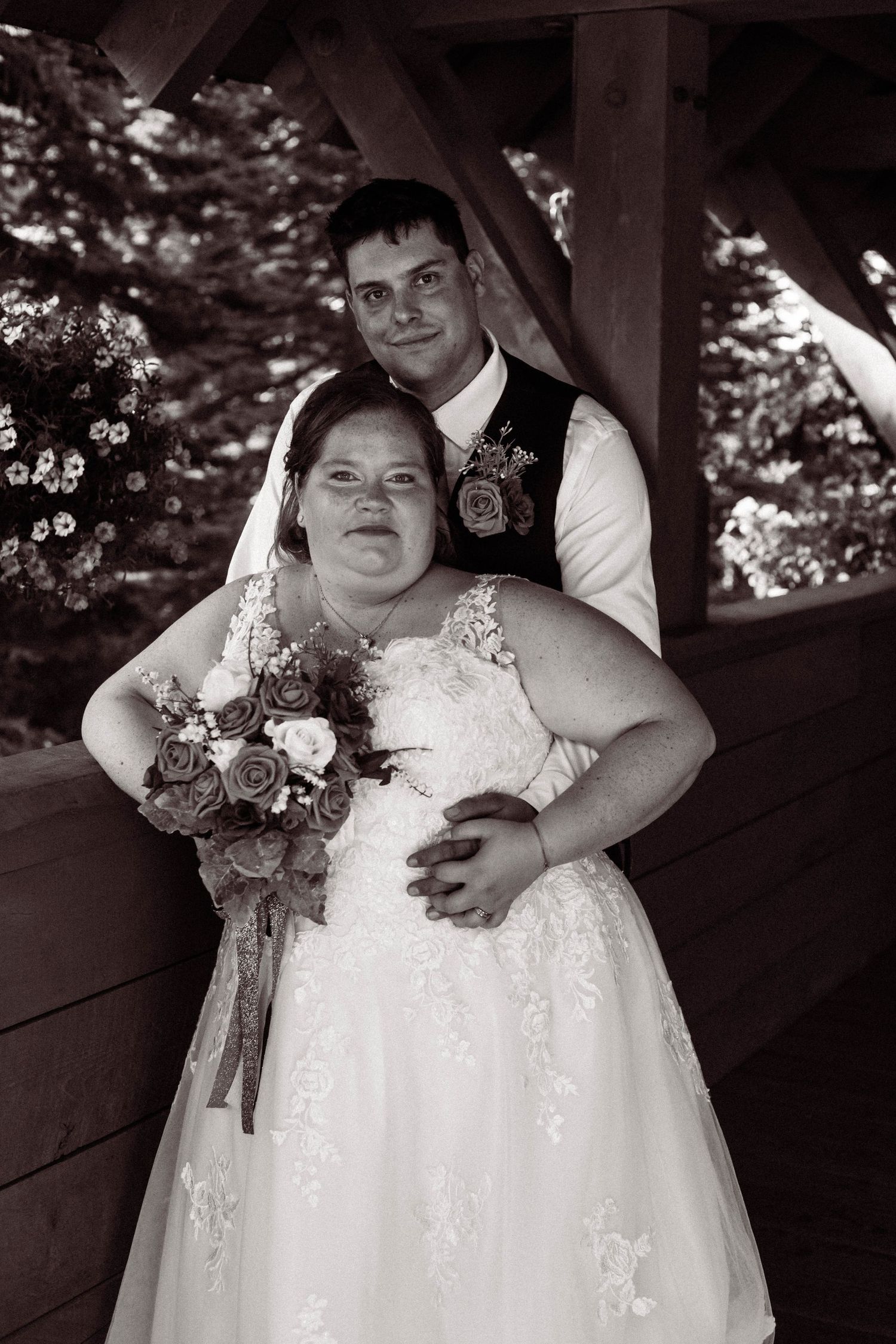 A bride and groom pose together in a rustic gazebo during their wedding, with the bride holding a floral bouquet.