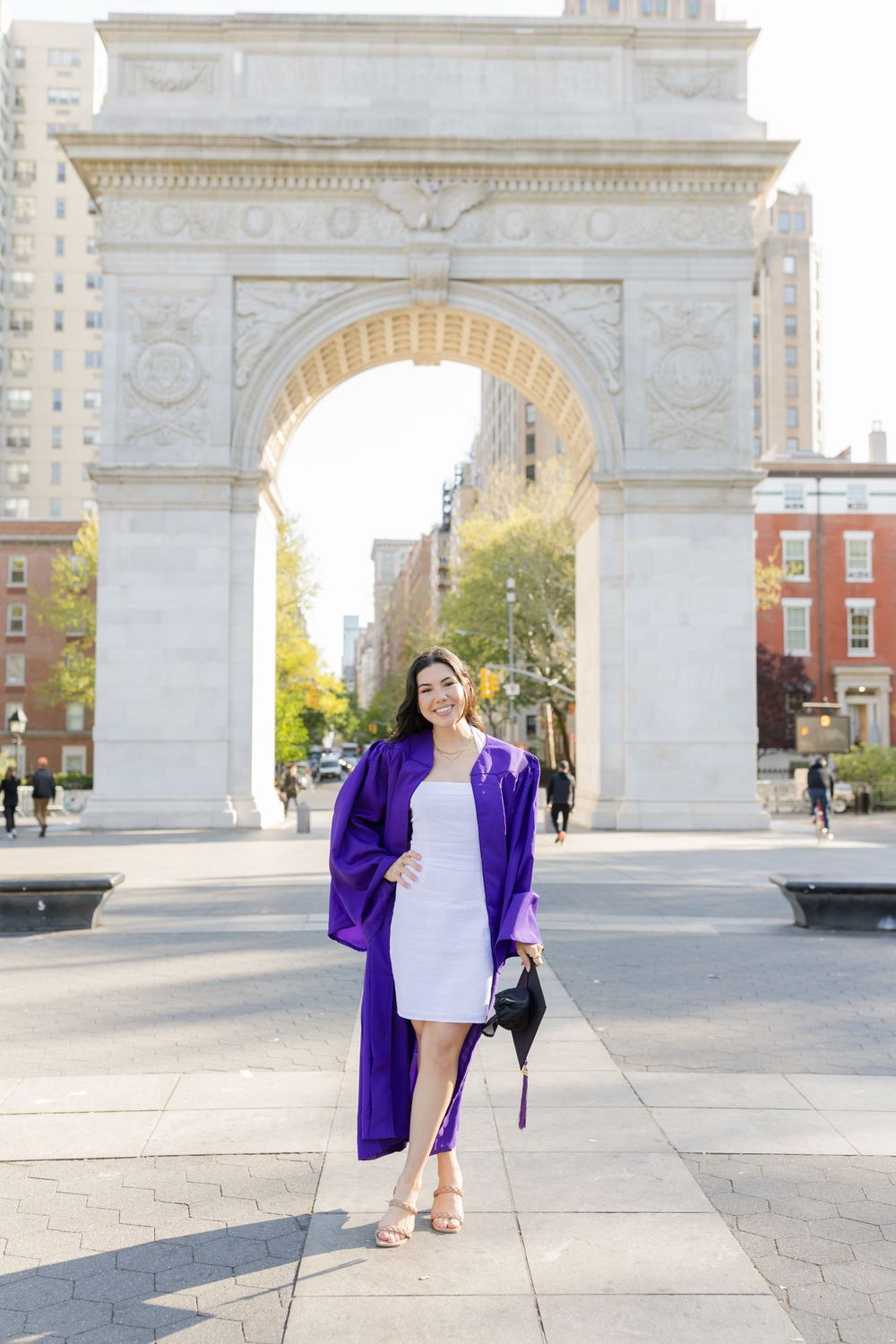 Graduate in purple and white walks confidently past Washington Square Arch.