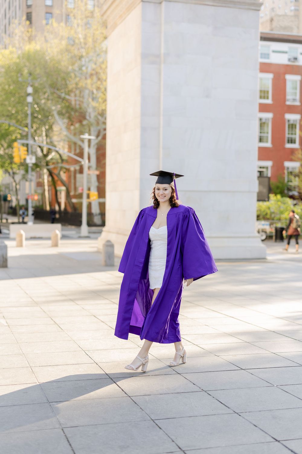 Graduate in purple graduation gown poses on campus.