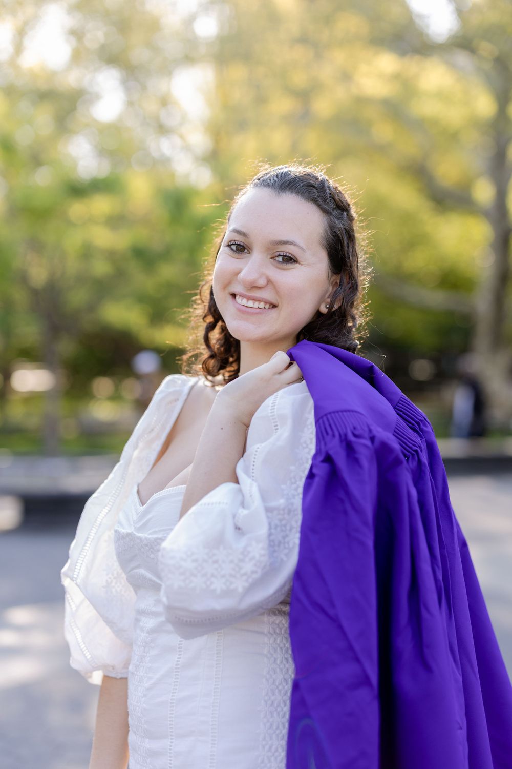 Graduate wearing purple graduation gown over white dress smiles at camera.