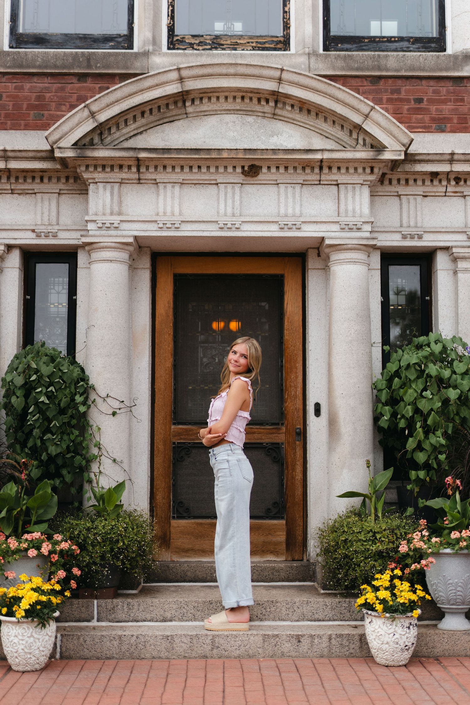 A person in a navy blue dress poses next to an ornate white fountain in a garden setting.