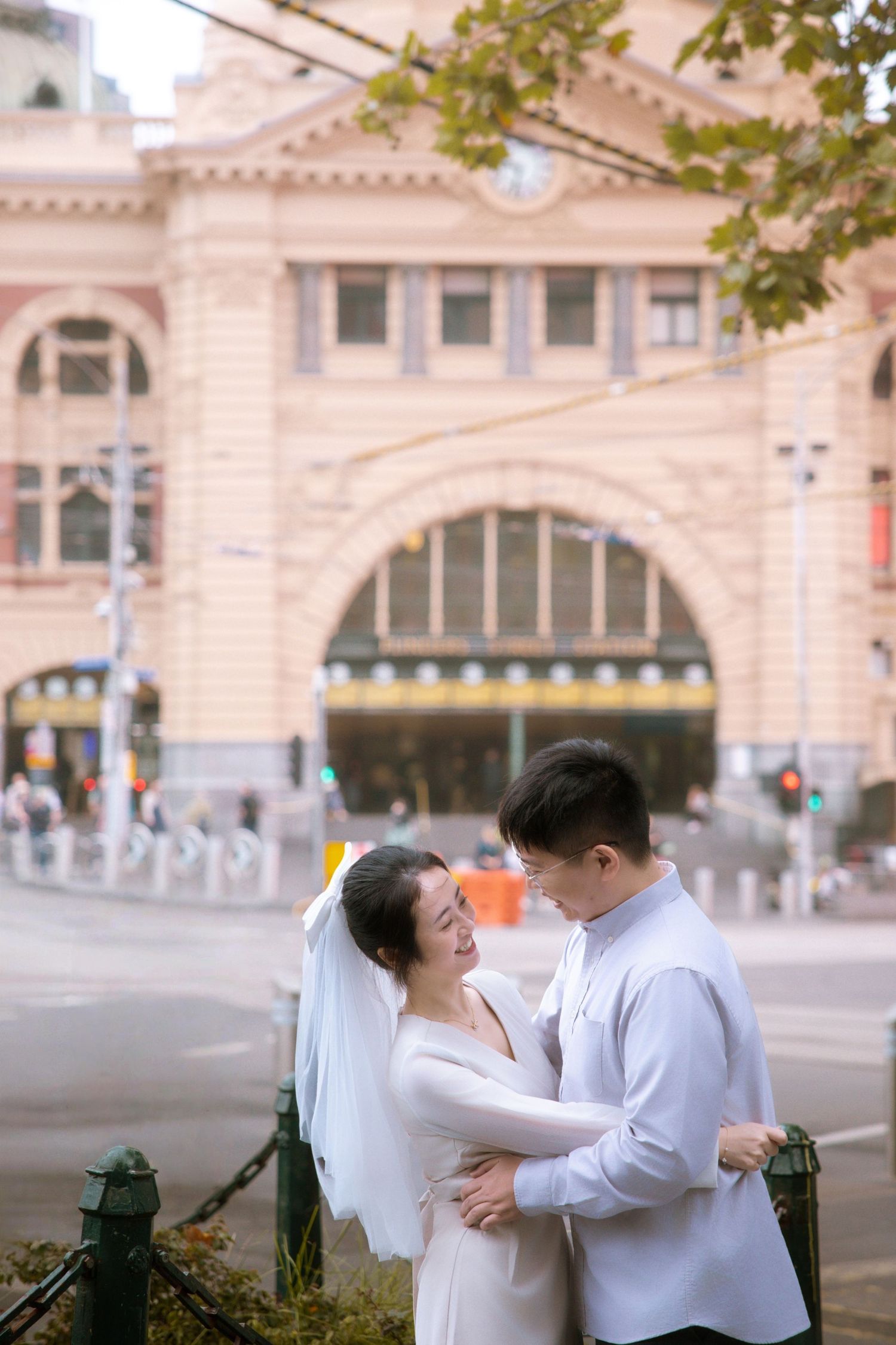 A tender moment between a couple in wedding attire outside Melbourne's Flinders Street Station.