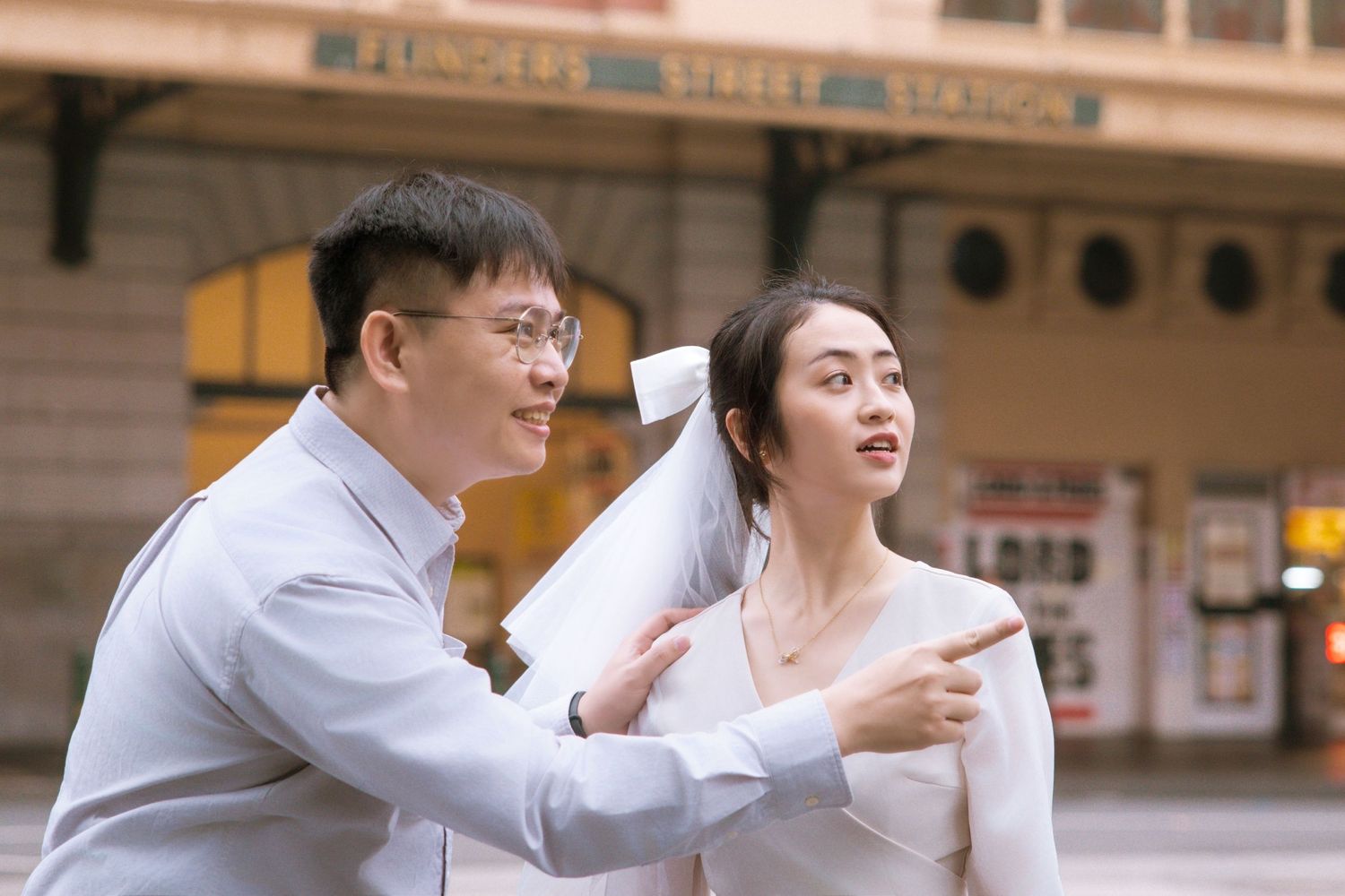 A joyful couple pointing and laughing outside the historic Flinders Street Station.