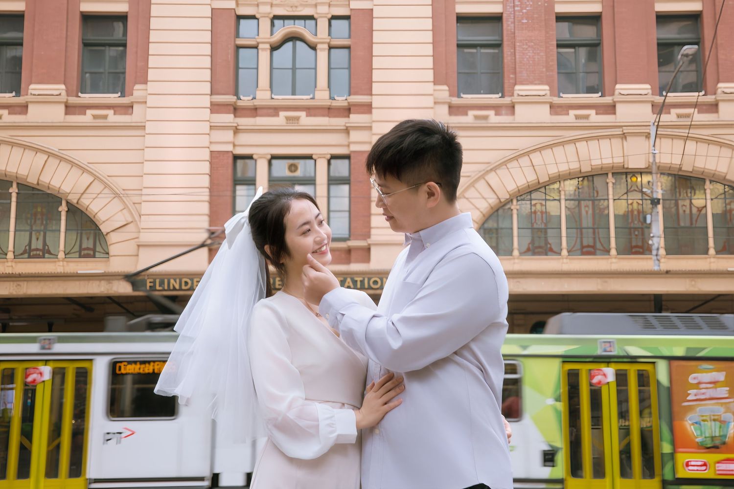 A romantic wedding couple embraces in front of a historic building with pink facade and arched windows.