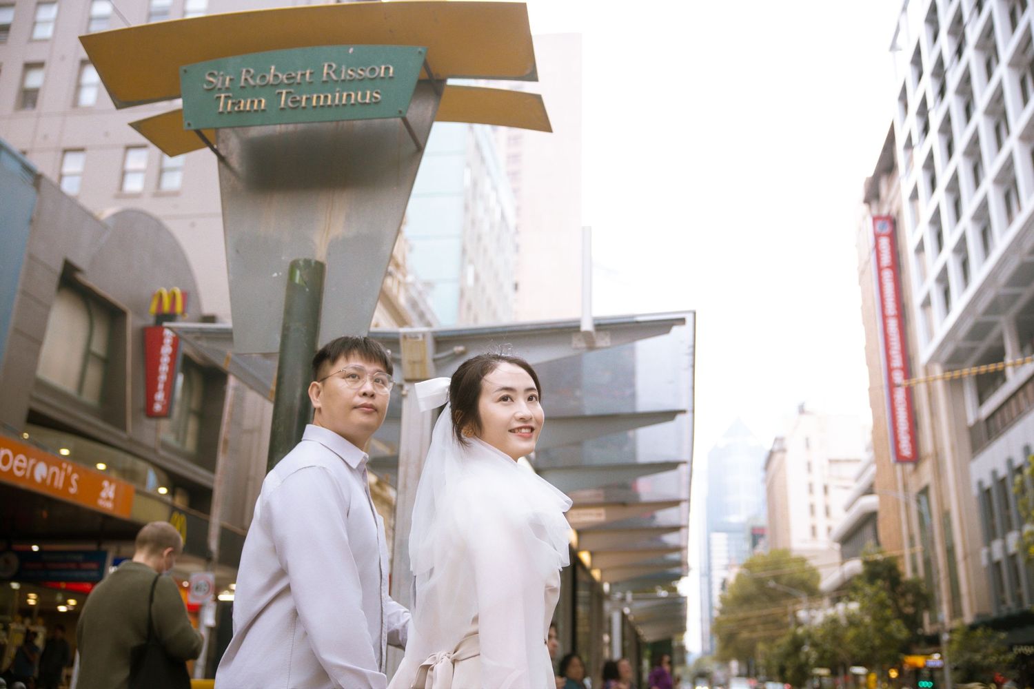 A couple in white outfits share a romantic moment on a city street with urban signage.