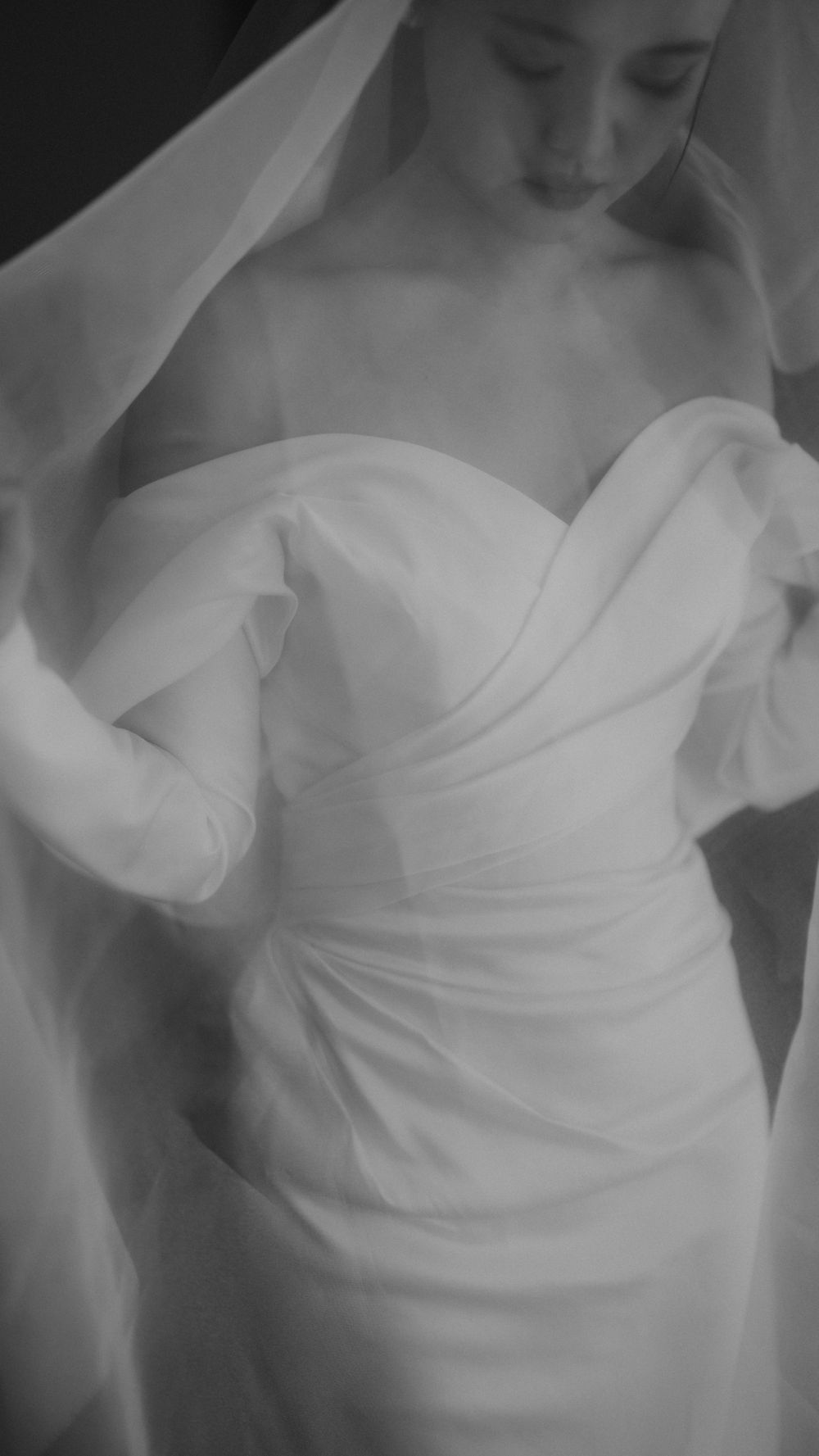 Close-up of draped white wedding gown with sweetheart neckline under delicate veil.