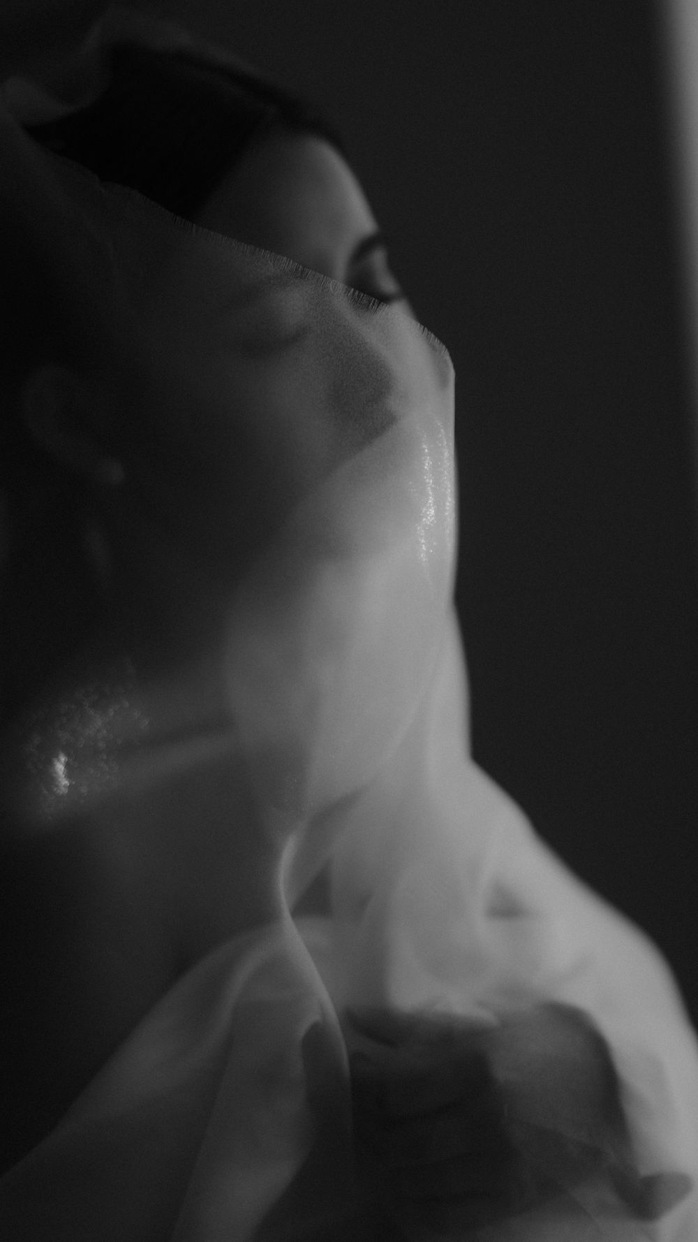Ethereal black and white portrait through translucent fabric creating mysterious atmosphere.