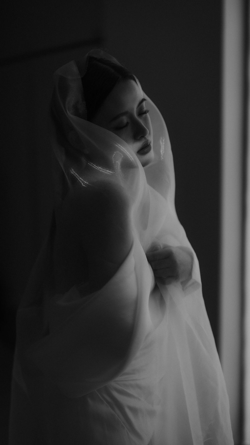 An artistic black and white bridal portrait with flowing veil creating a dreamy silhouette.