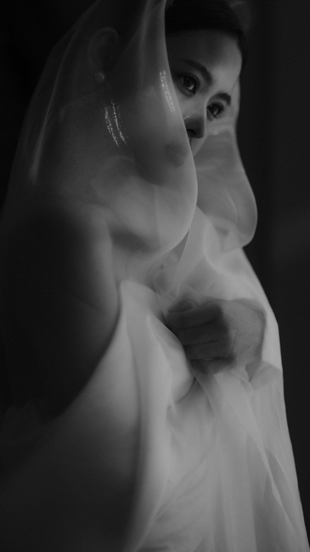 Ethereal black and white portrait through a flowing sheer bridal veil creating a dreamy effect.