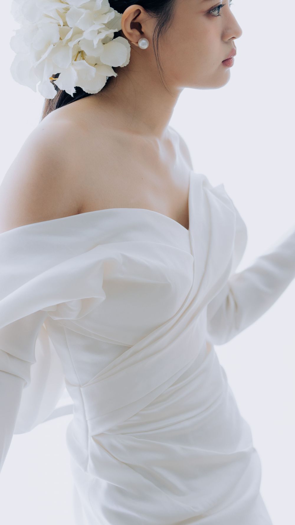 Elegant bridal portrait featuring white orchid hair accessory and draped off-shoulder wedding gown in soft lighting.