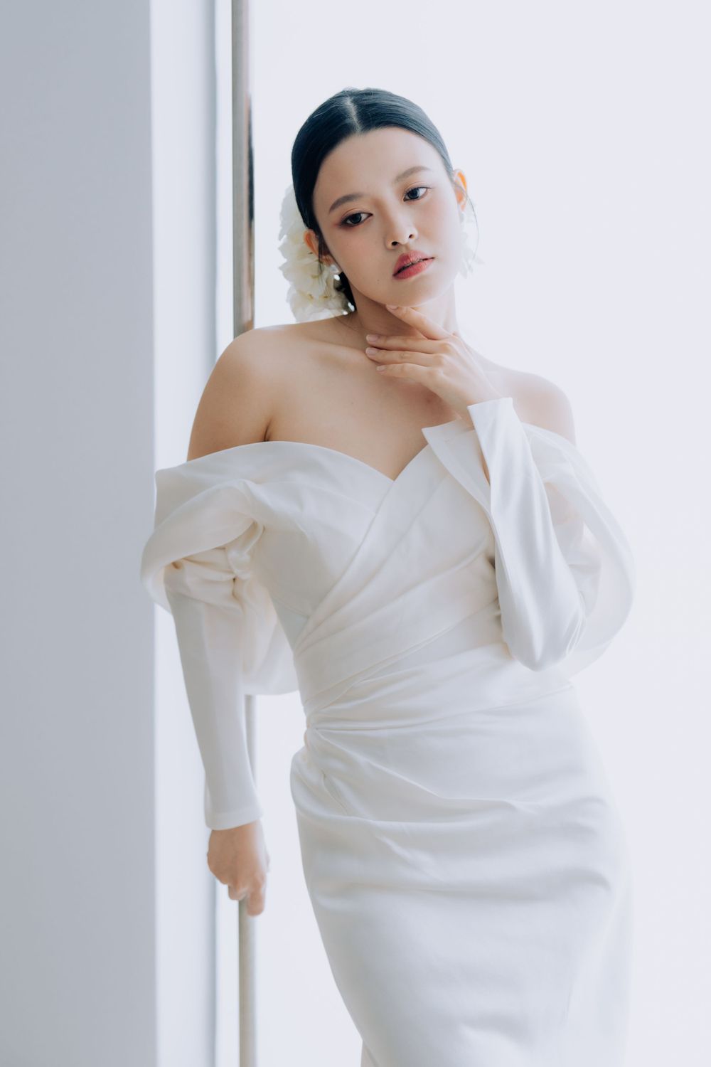 Elegant off-shoulder white wedding gown with ruched detailing in minimalist studio setting.