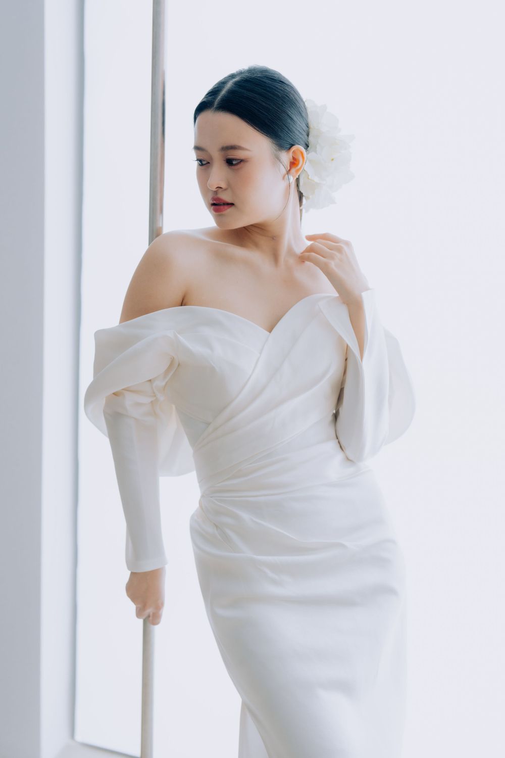 An elegant off-shoulder wedding dress with long sleeves and a fitted silhouette photographed in a bright studio setting.