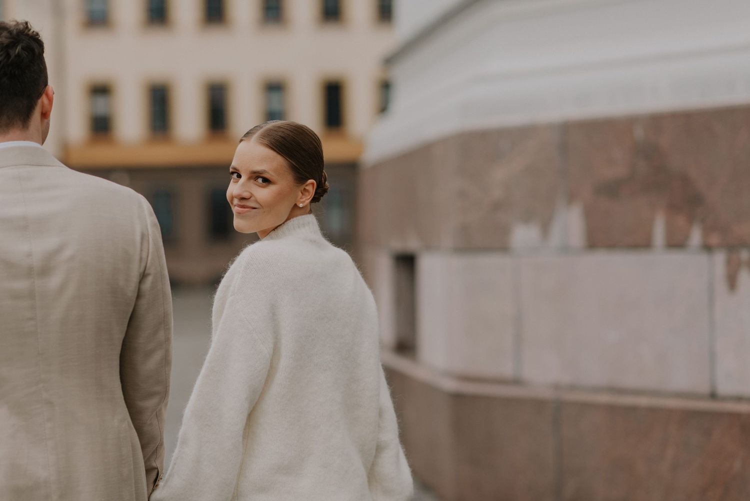 Elegant couple in winter white attire standing near urban architecture.