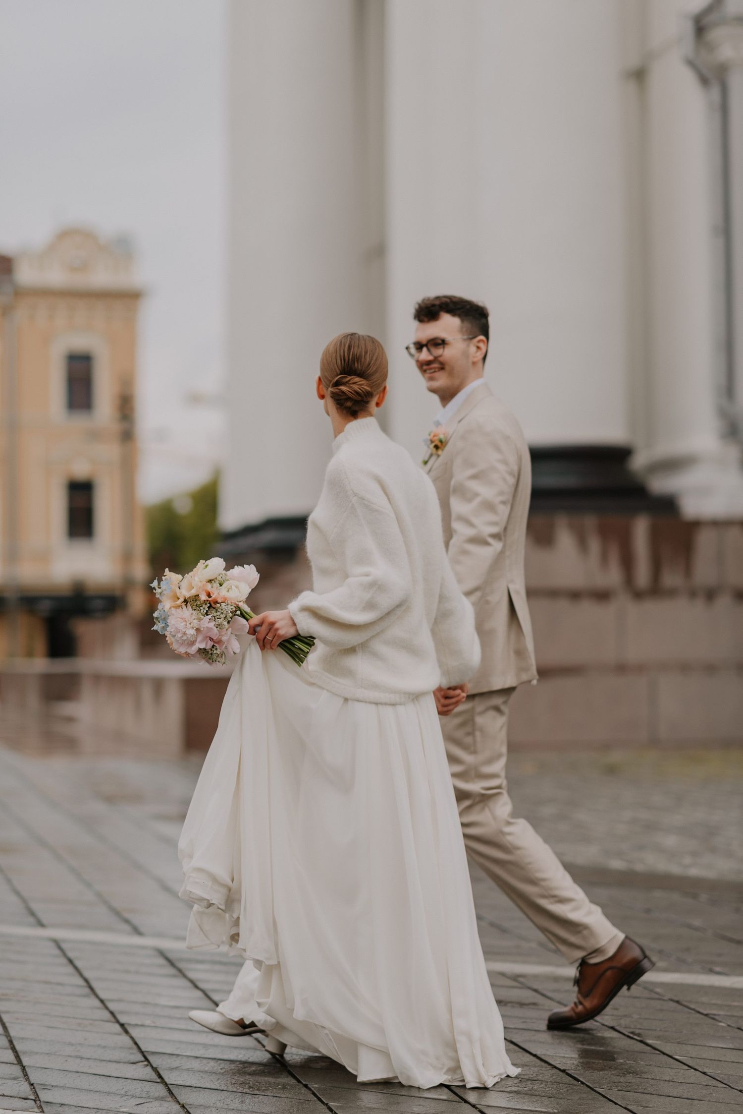 Wedding couple walking together on a rainy day in light-colored attire.