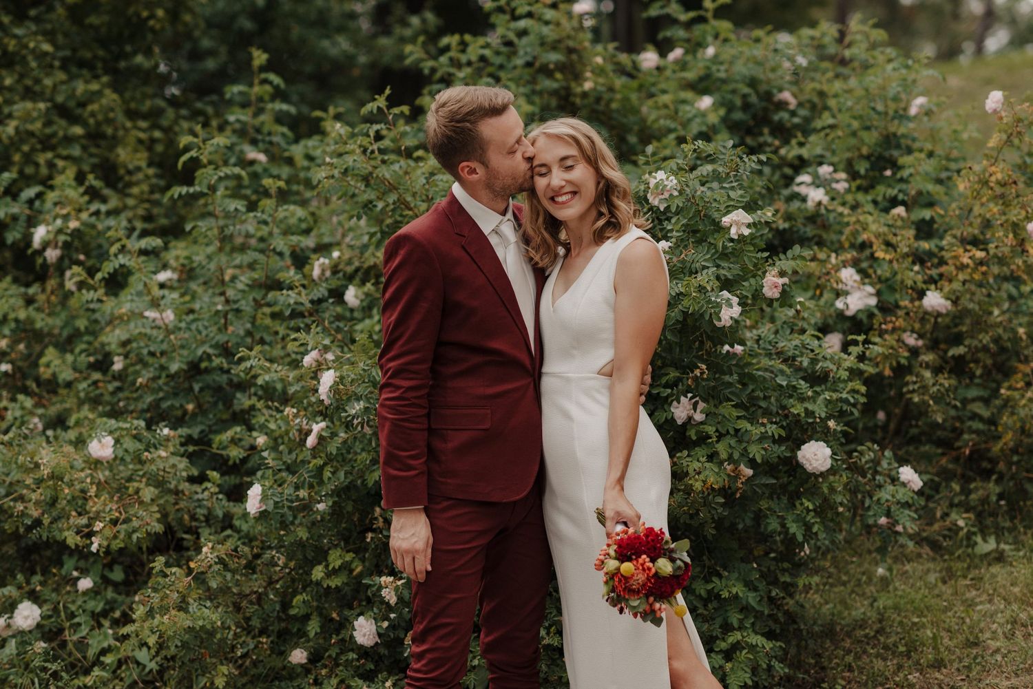Wedding couple sharing intimate moment in a blooming rose garden.