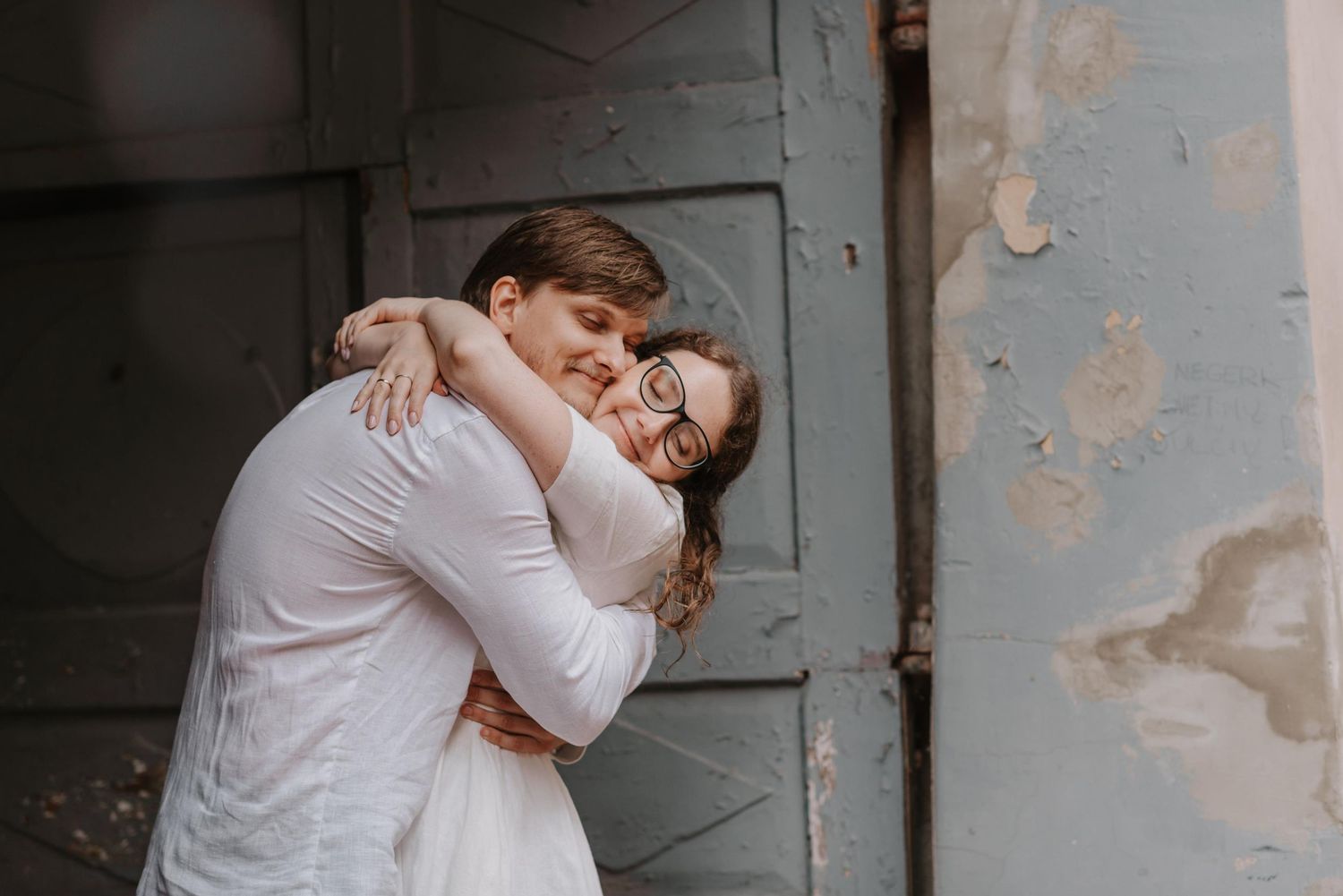 Intimate couple portraits against weathered grey walls show tender embraces.
