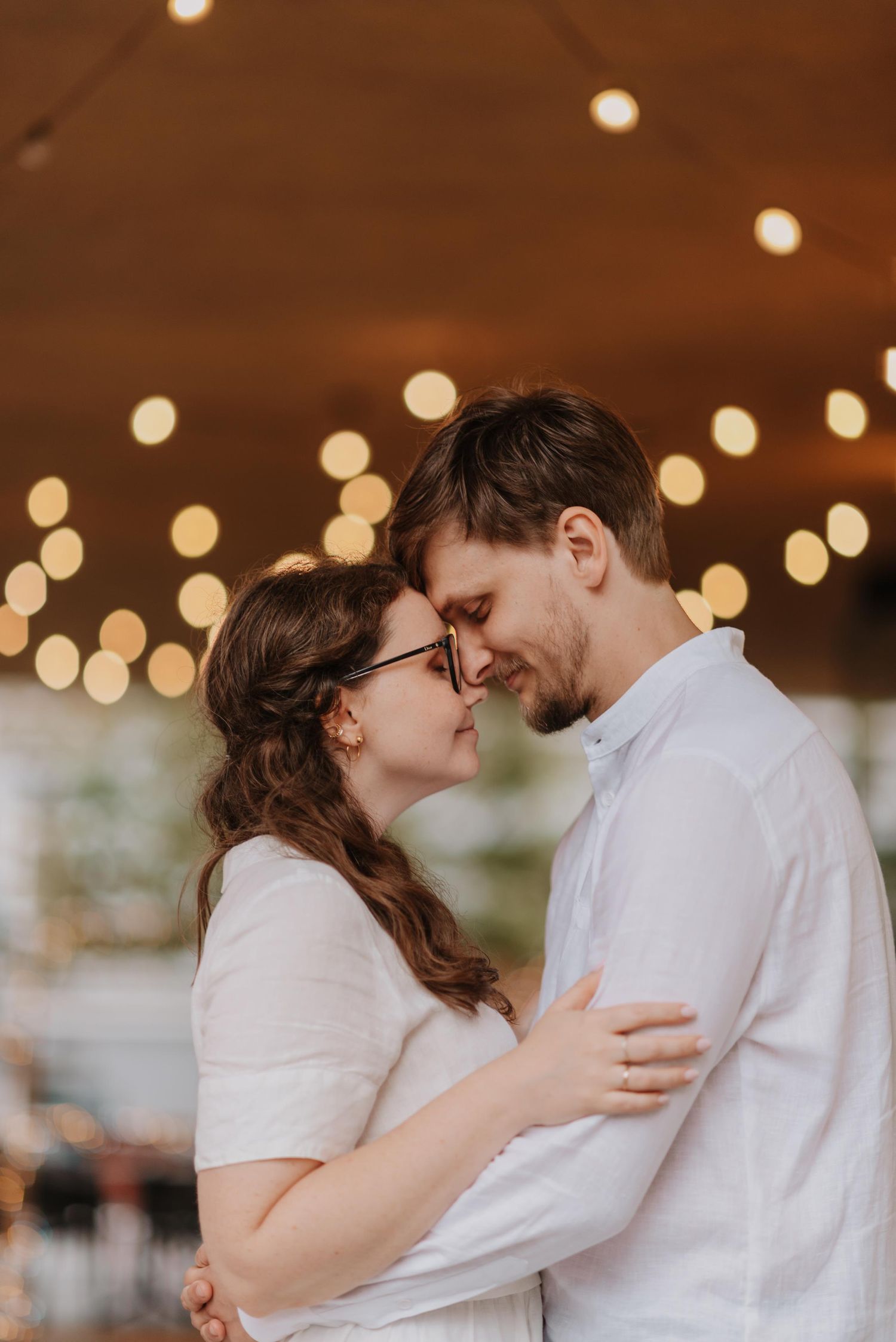 Indoor wedding portraits with warm string lights create romantic bokeh effect.