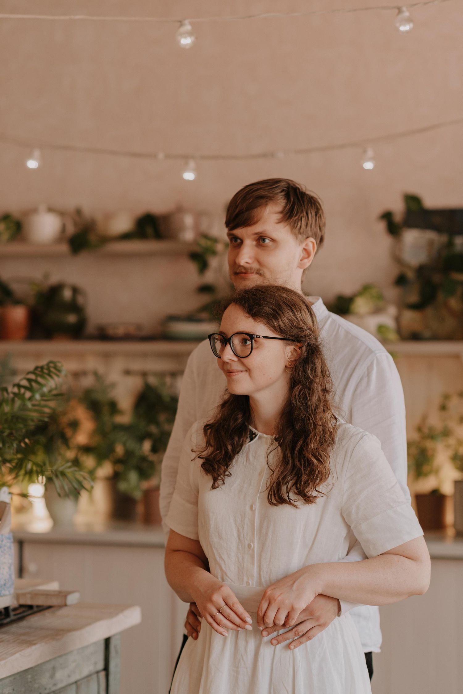 Couple sharing an intimate moment in a rustic indoor setting with hanging lights and plants.