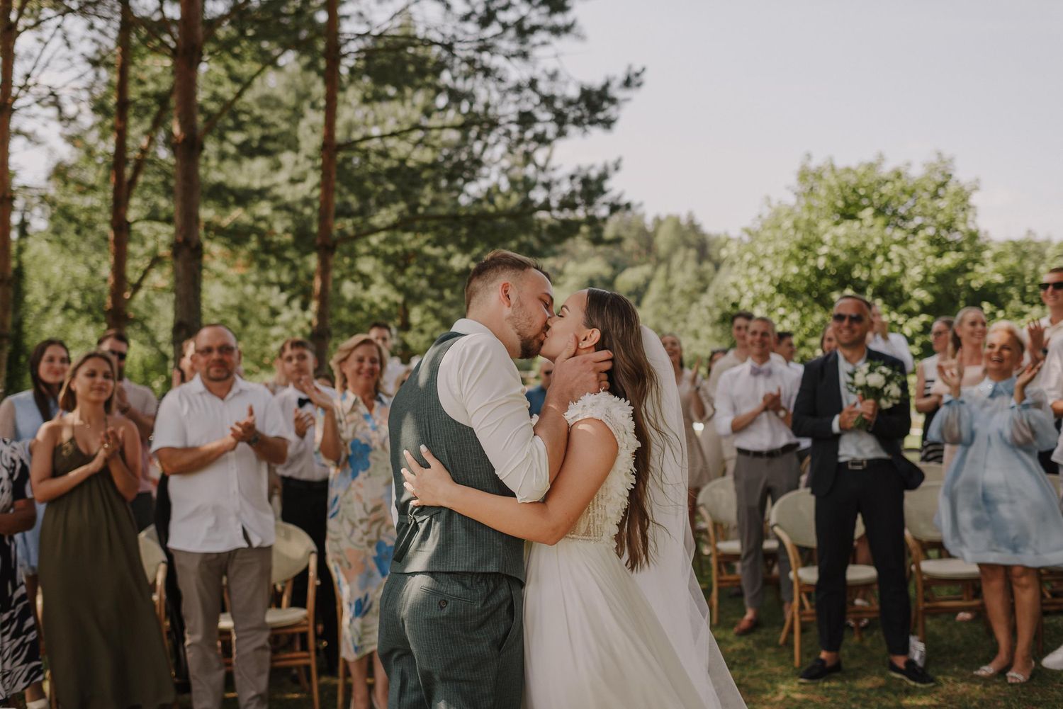 Outdoor wedding ceremony surrounded by pine trees with guests watching the celebration.