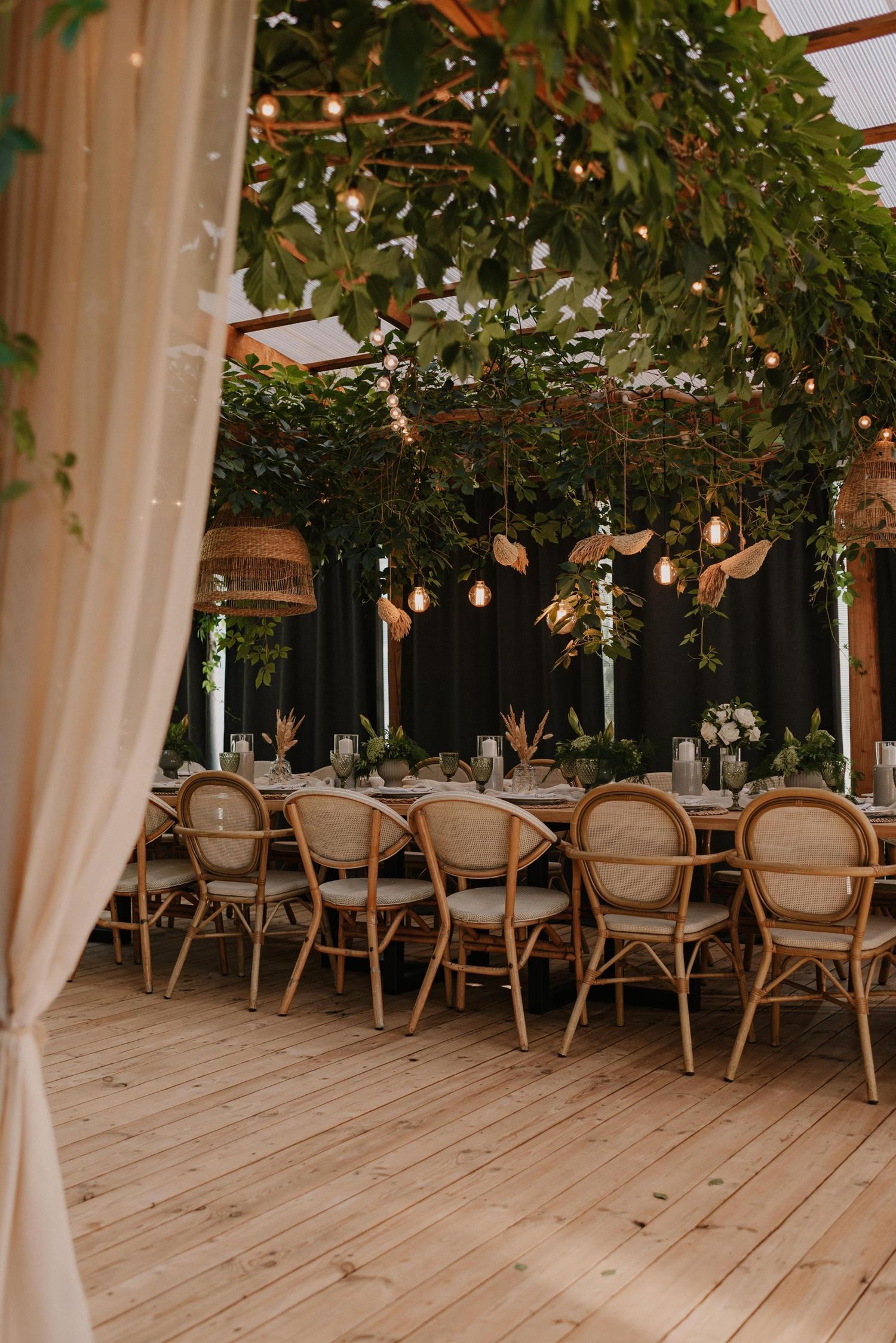 Rustic wedding venue with wooden chairs and hanging greenery under draped white fabric.