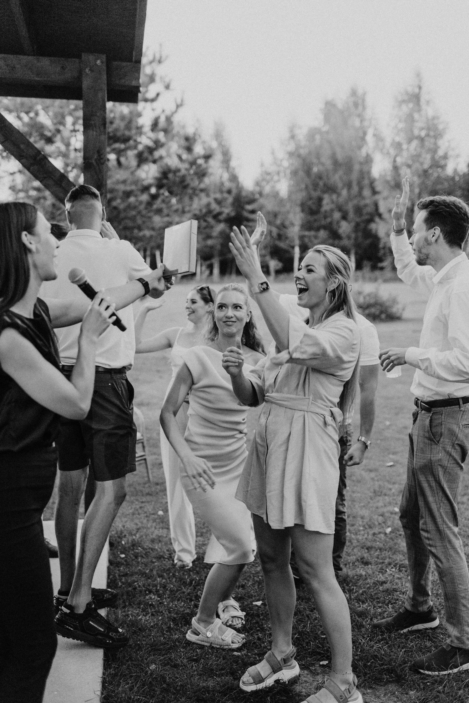 Black and white photo of lively wedding guests dancing and celebrating outdoors.