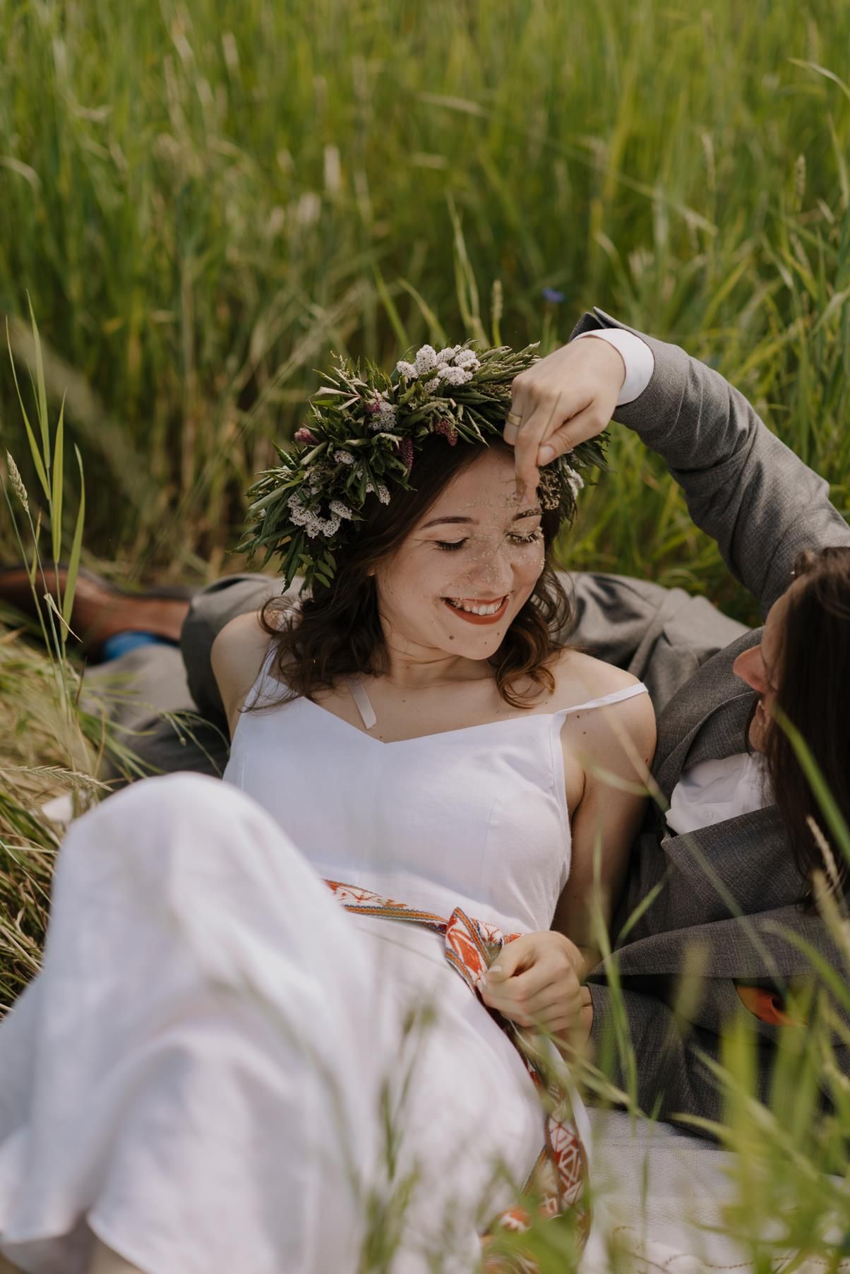 Bride wearing floral crown lying in tall grass field wearing white dress.