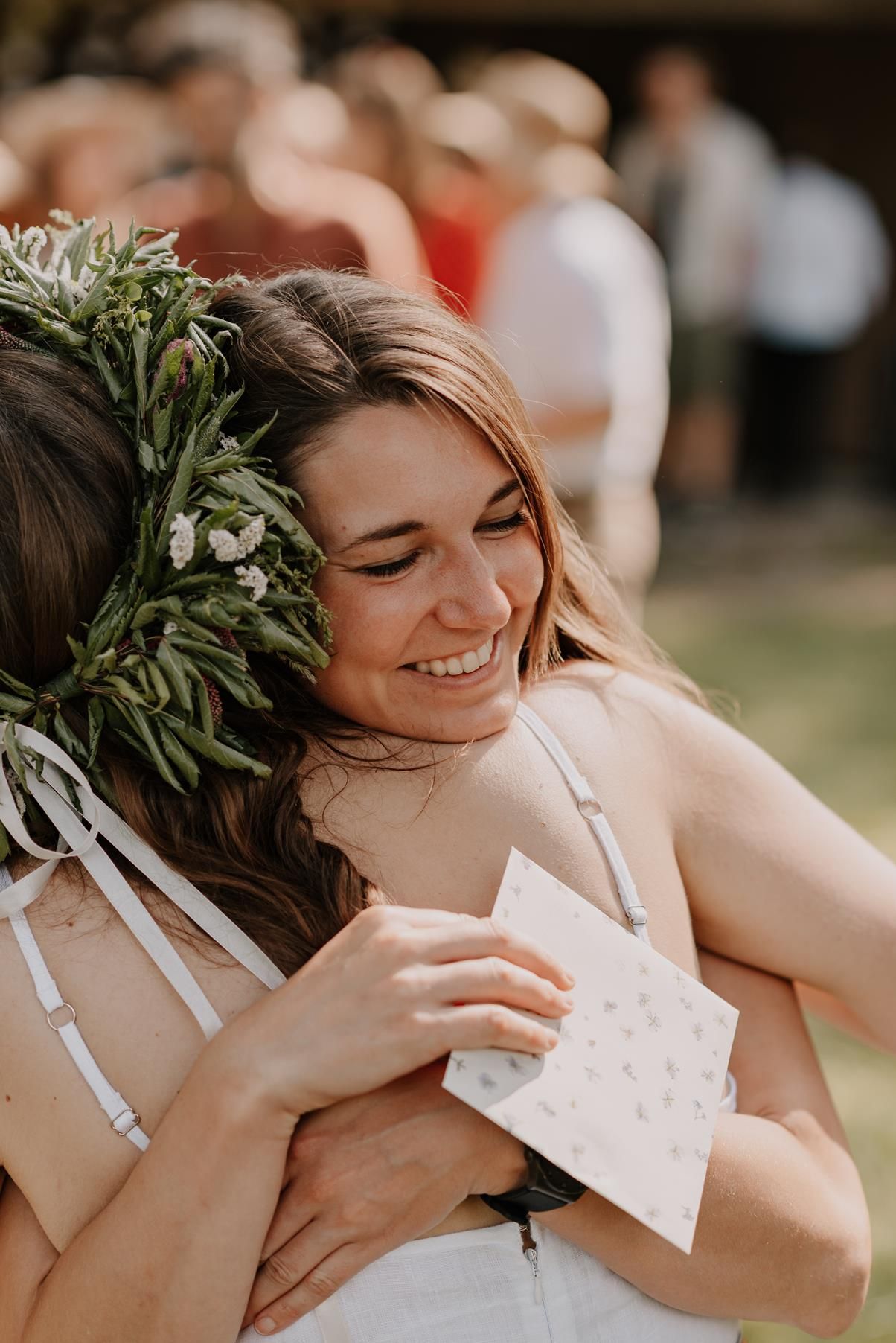 Happy person wearing floral crown holding card at outdoor celebration.