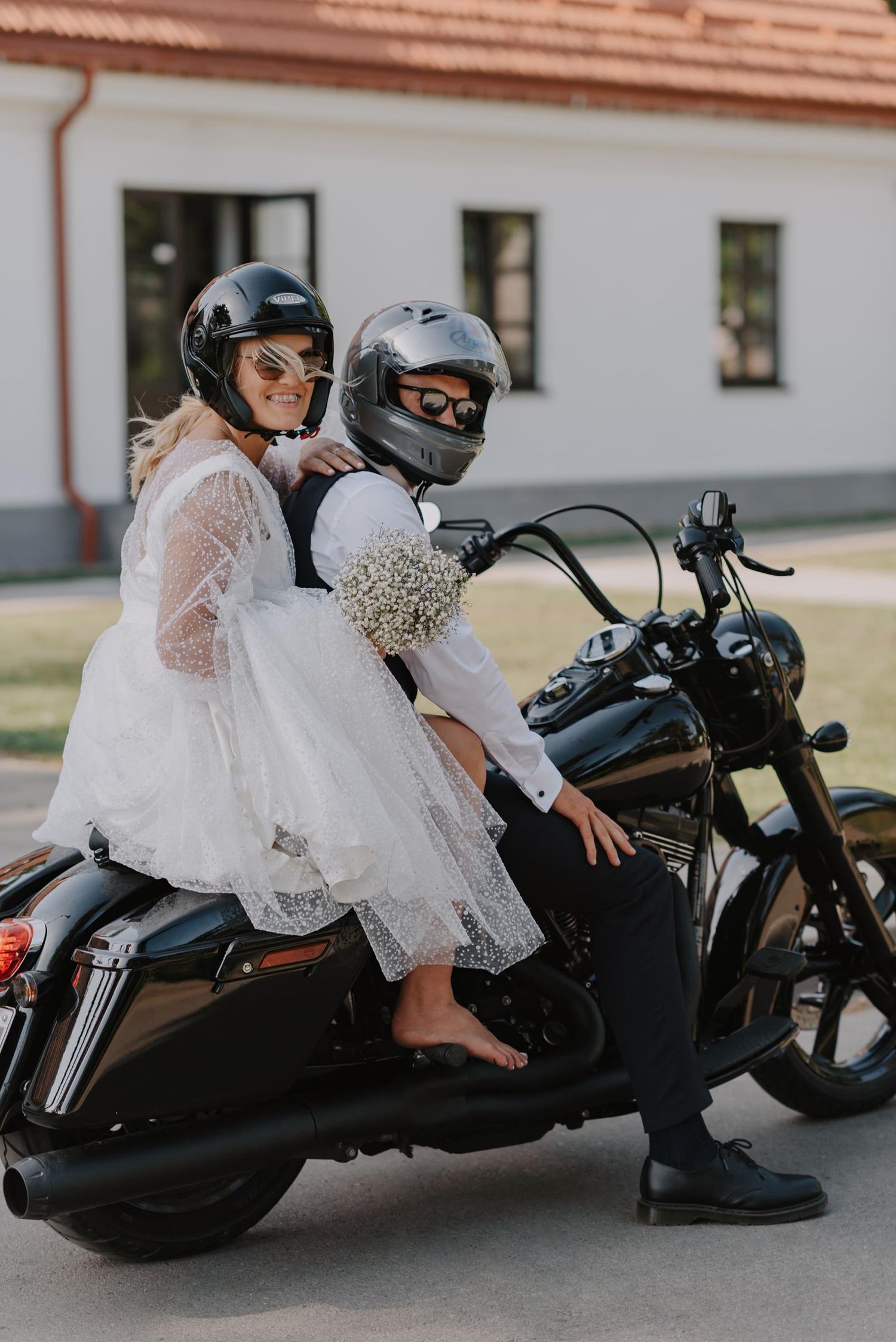 Person wearing white lace dress sits on black motorcycle making poses.