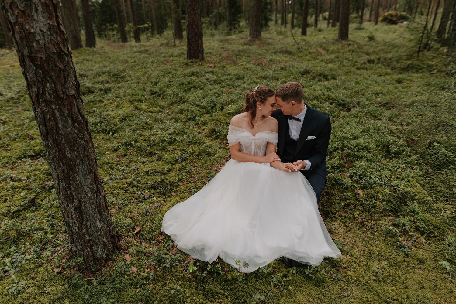 Couple in wedding attire sitting together on a bench in a peaceful forest setting.