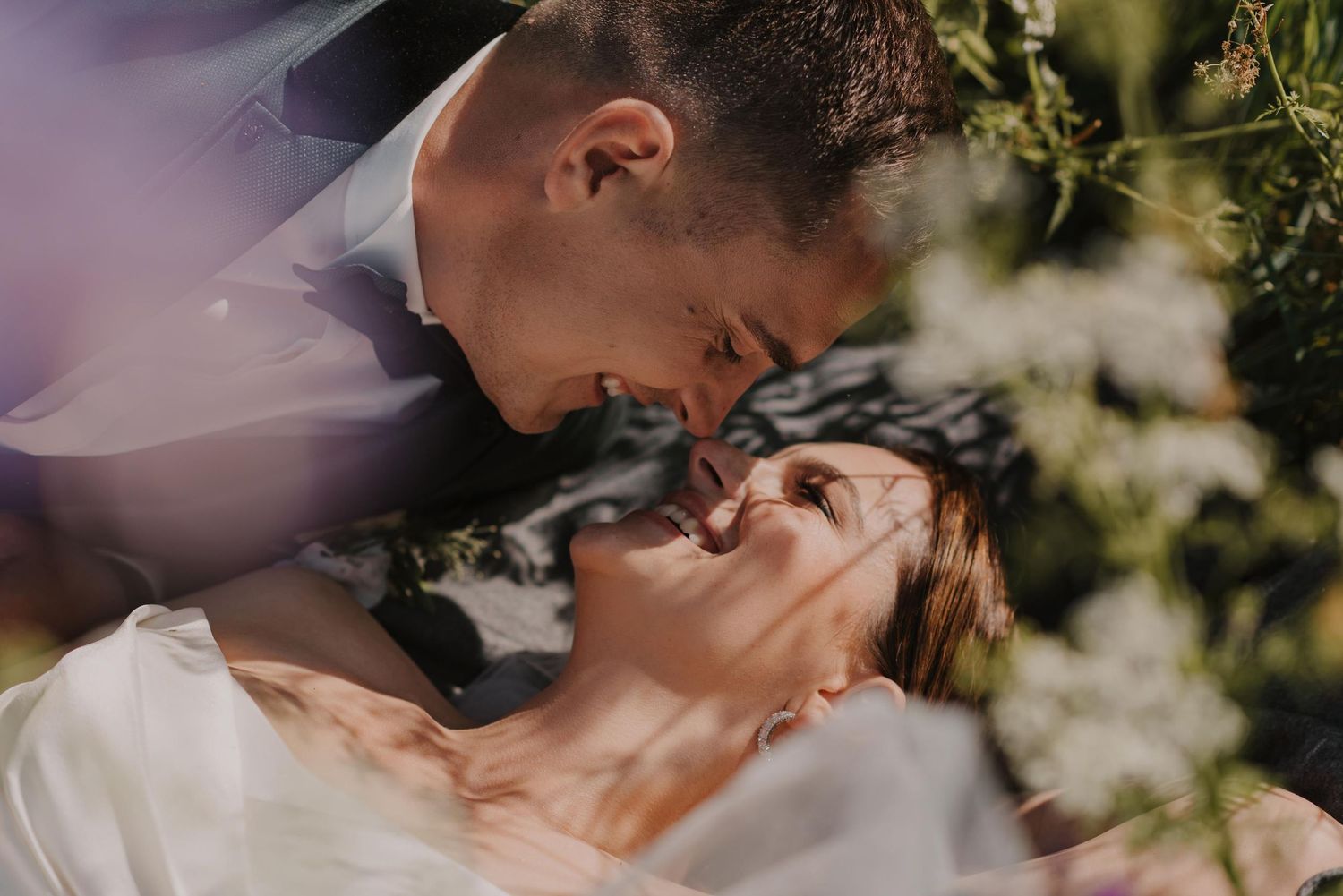 A romantic wedding couple embracing outdoors in a sunlit garden setting.