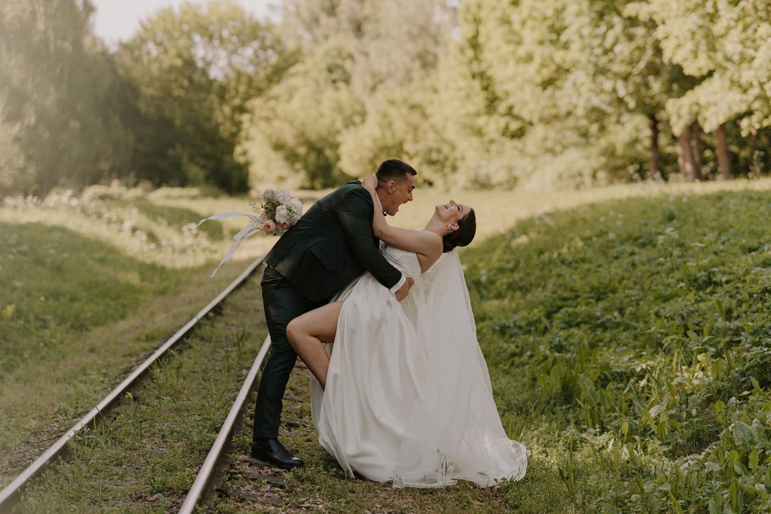 A tender wedding moment captured on a grassy hill with sunlight filtering through trees.