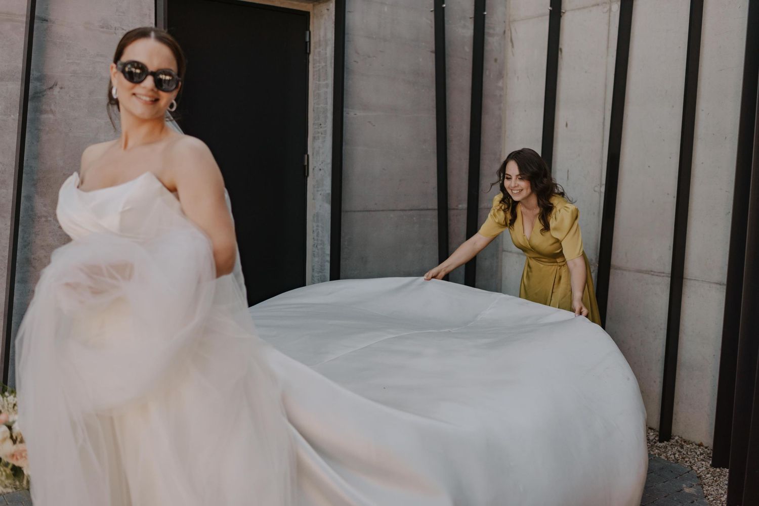 A bride in a flowing white dress twirls against an industrial backdrop.