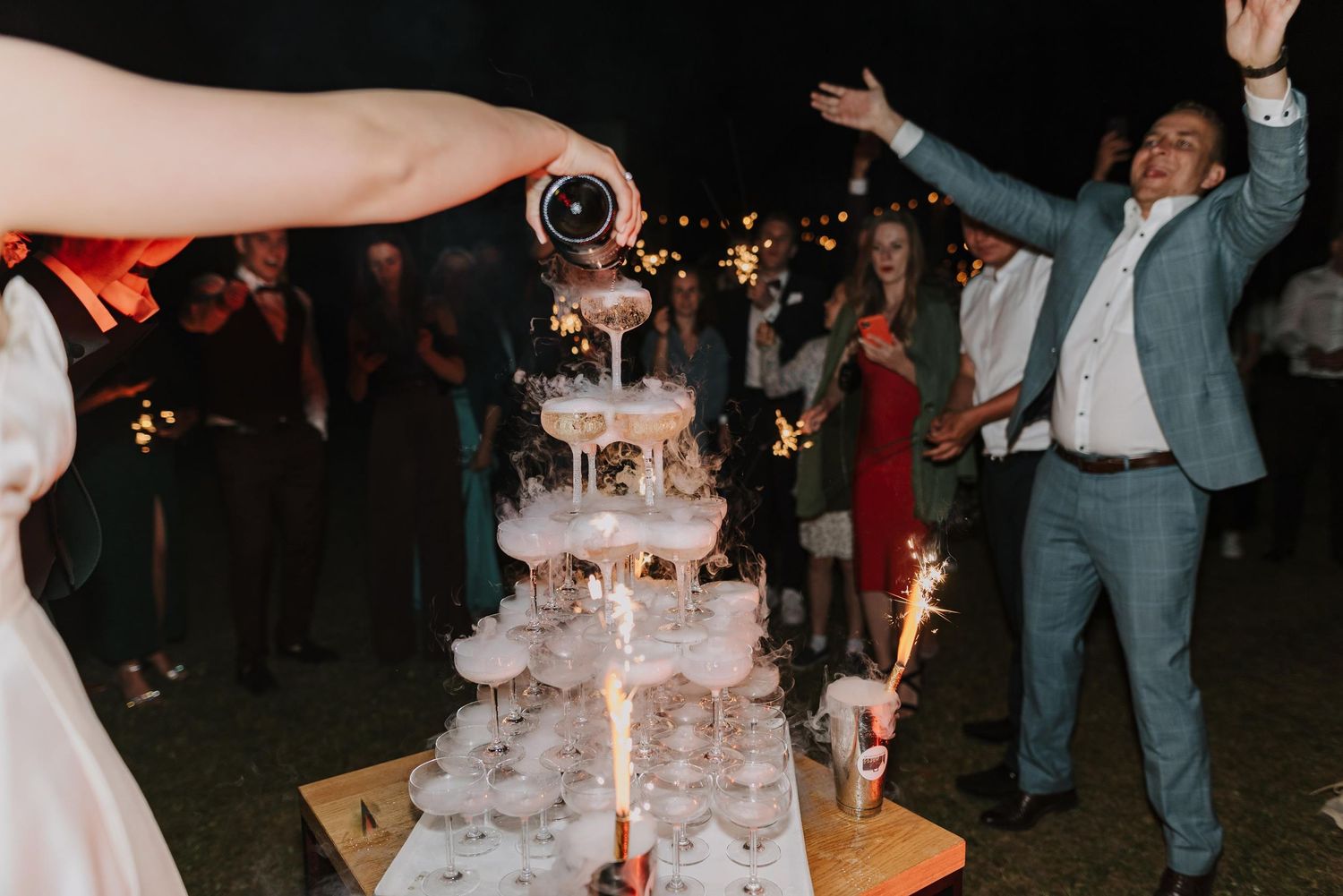 A wedding reception at night with a tiered cake and celebrating guests.