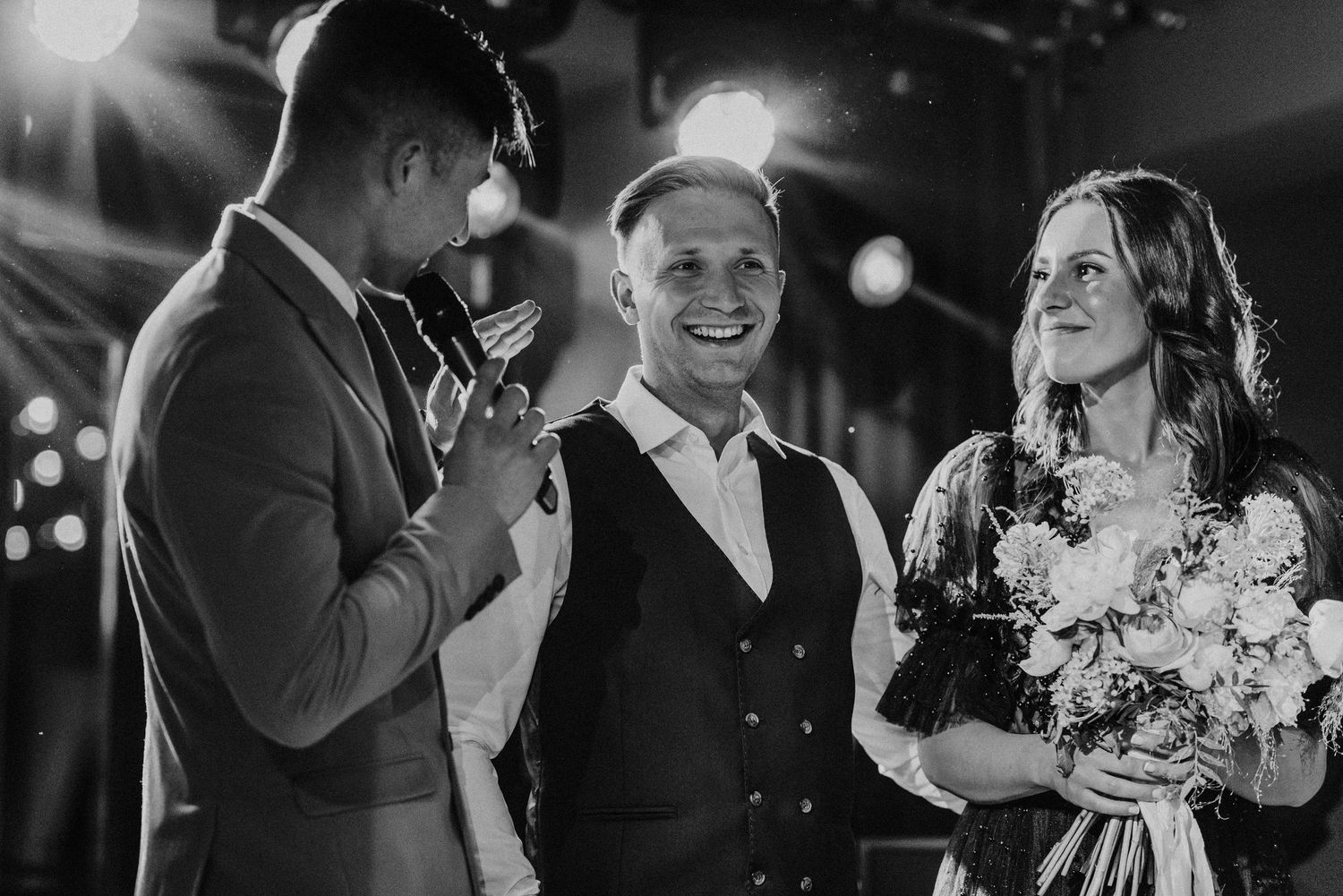 Black and white photo showing couples dancing and celebrating at an indoor reception party.