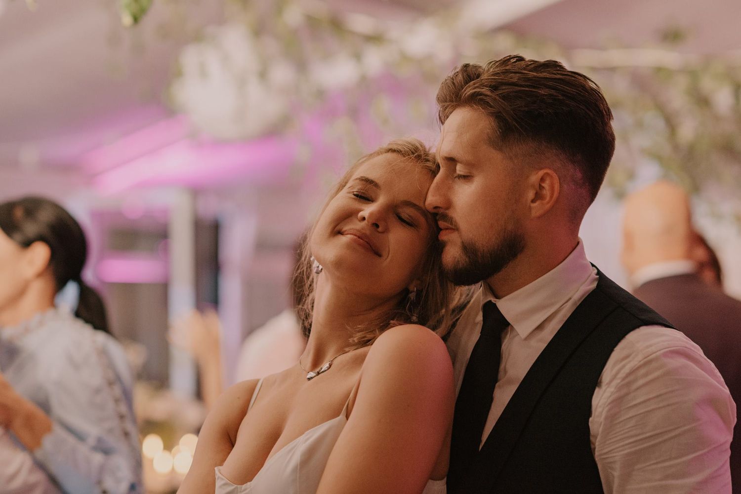 Romantic dance sequence at a wedding reception with couples dancing under pink mood lighting.