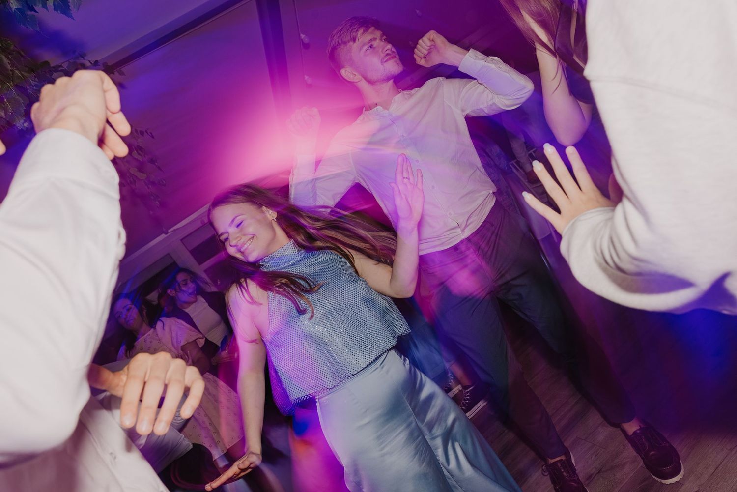 Wedding guests dancing on a crowded dance floor illuminated by purple and blue lighting.