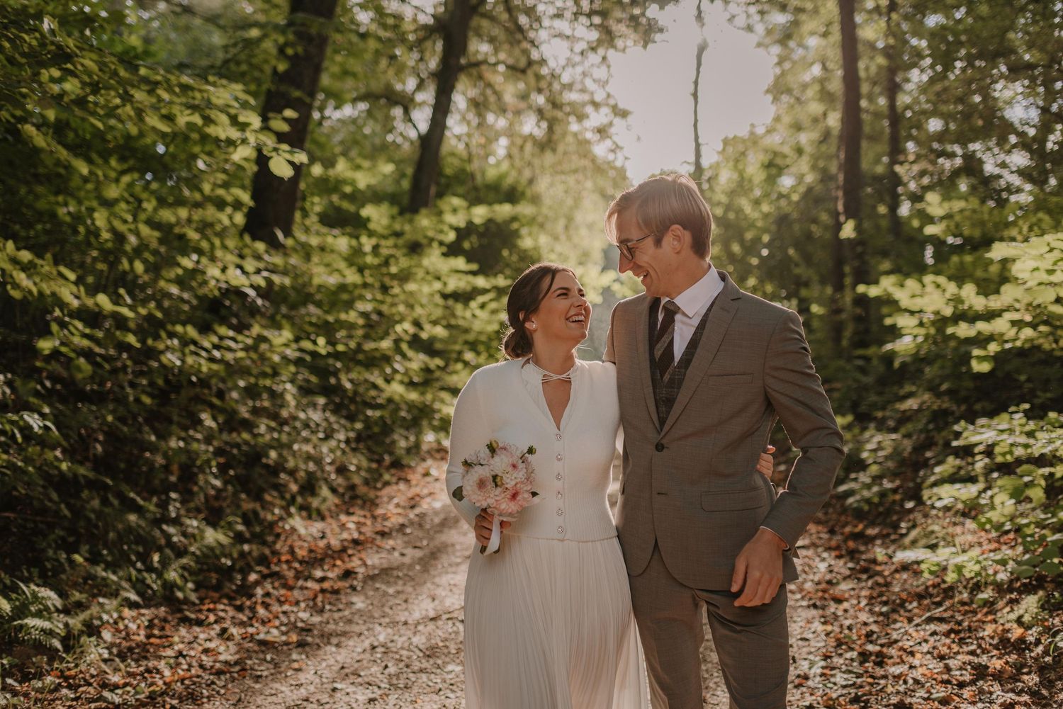 A romantic wedding ceremony takes place in a sunlit forest setting with beautiful natural greenery.