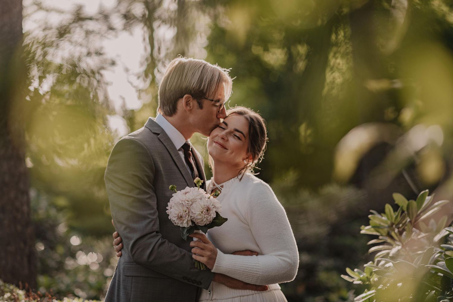Romantic wedding portraits taken outdoors with soft bokeh and natural sunlight filtering through trees.