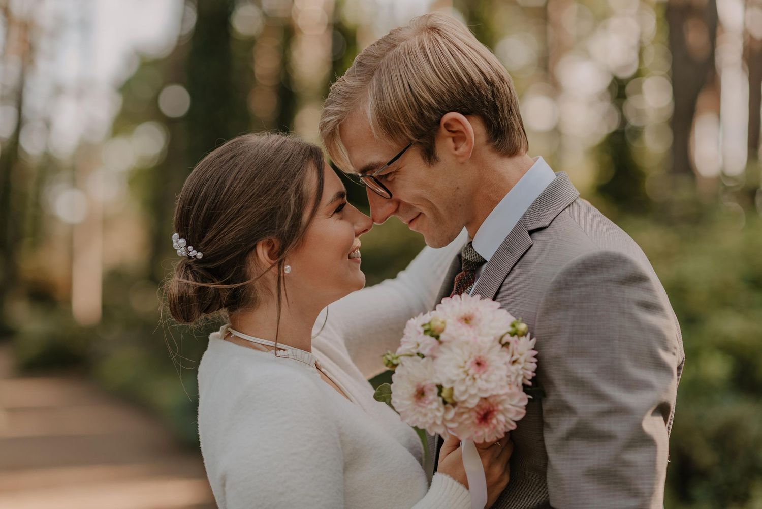 A couple shares an intimate moment against a backdrop of lush trees and dappled sunlight.